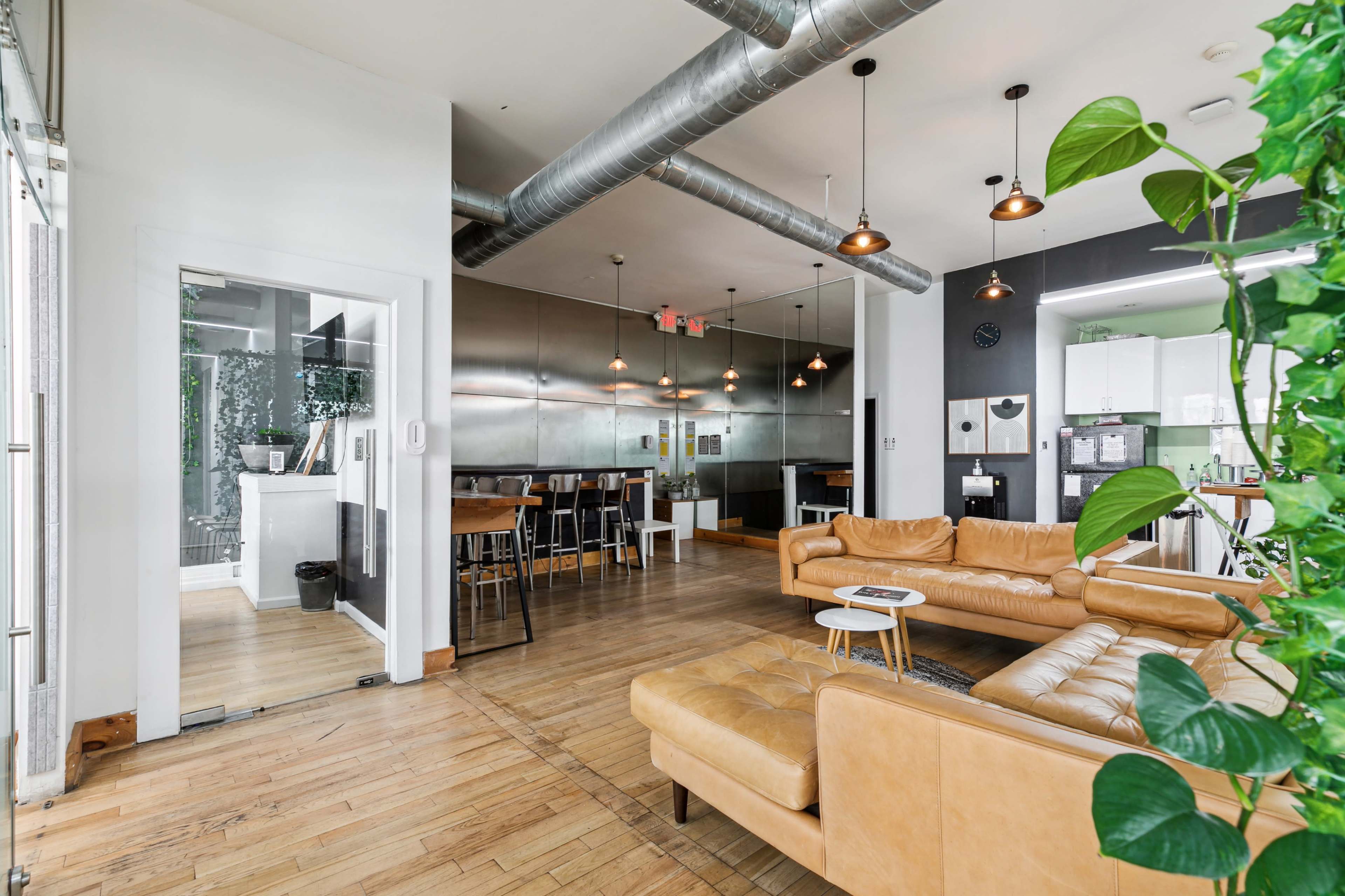 The image shows a modern open-concept living space featuring a leather sofa, a dining area with barstools, and a kitchen with stainless steel appliances.