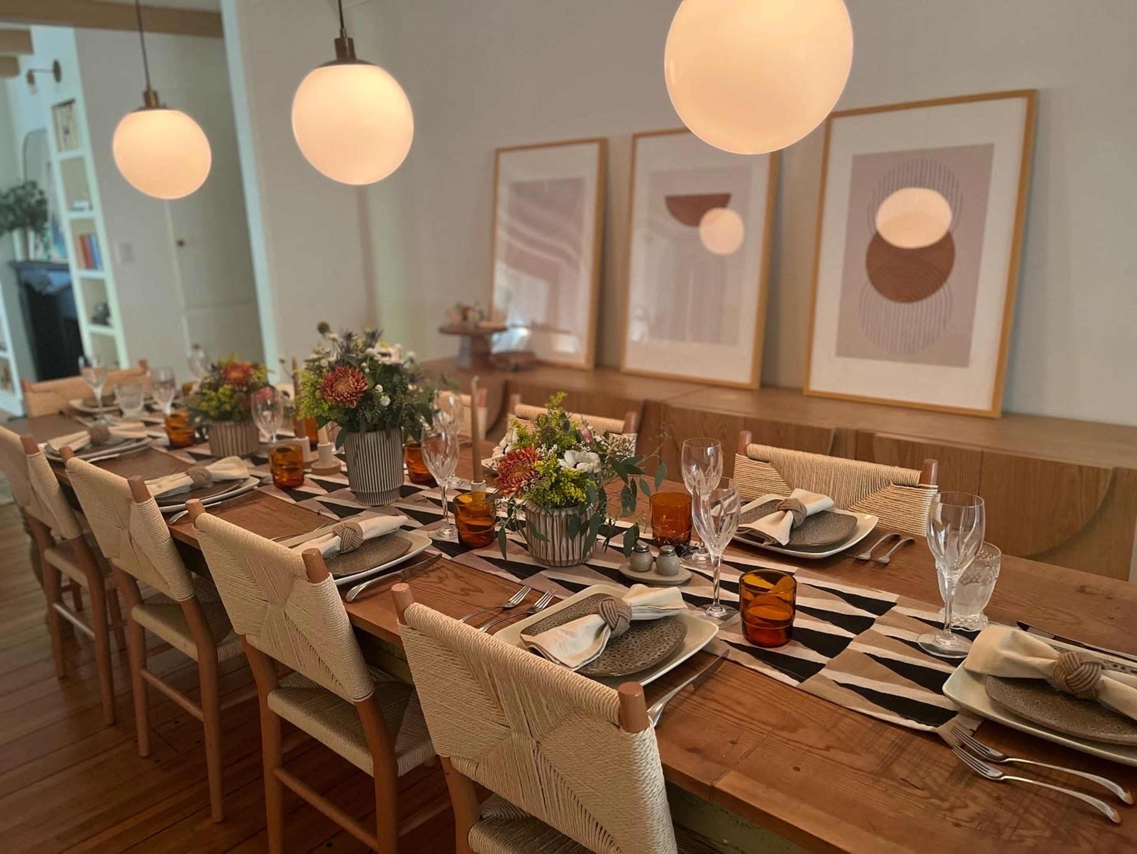 A long dining table is set with plates, glasses, and floral centerpieces, surrounded by modern decor and artwork on the walls.