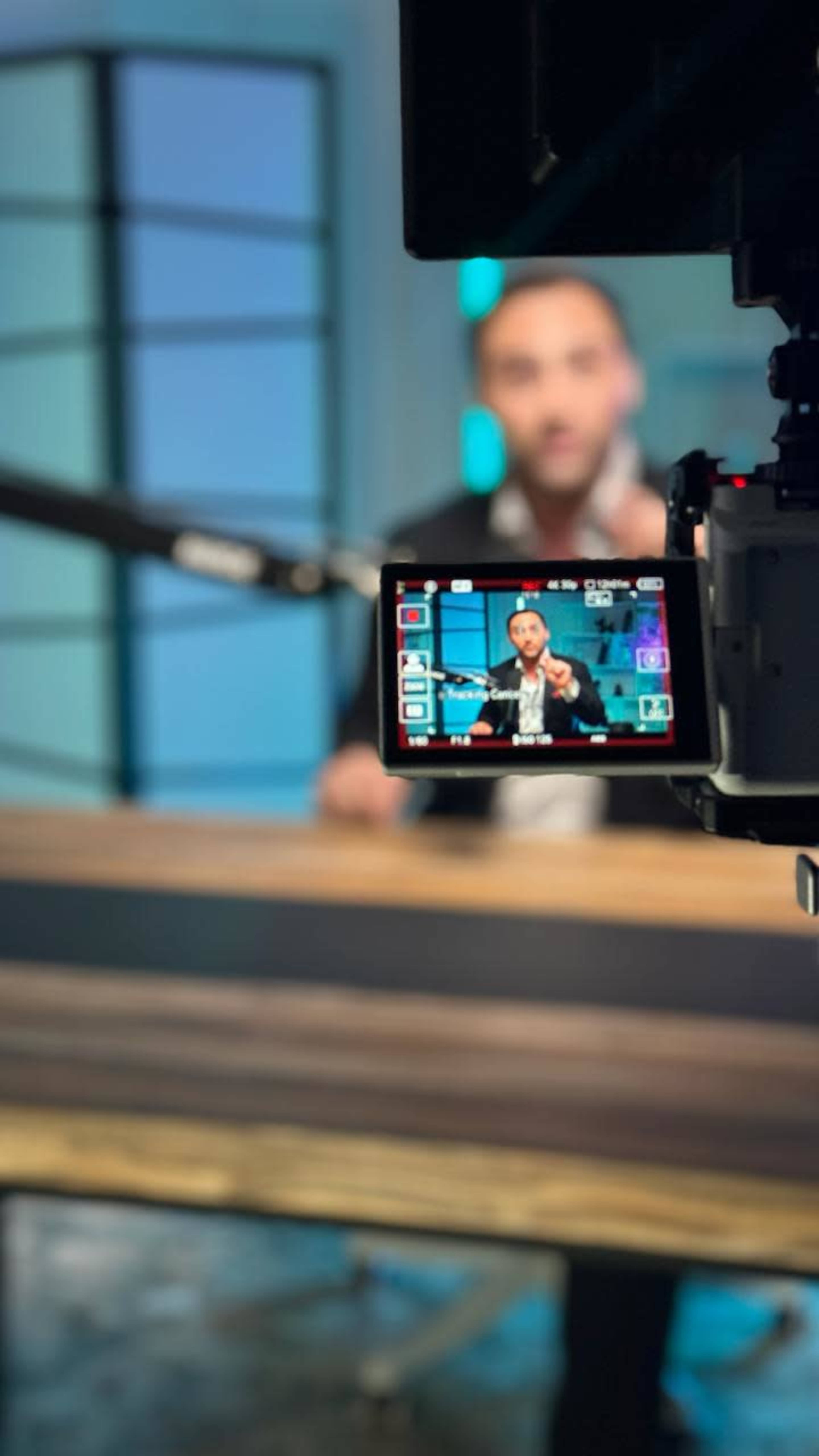 A camera captures a person speaking at a table in a studio setting.