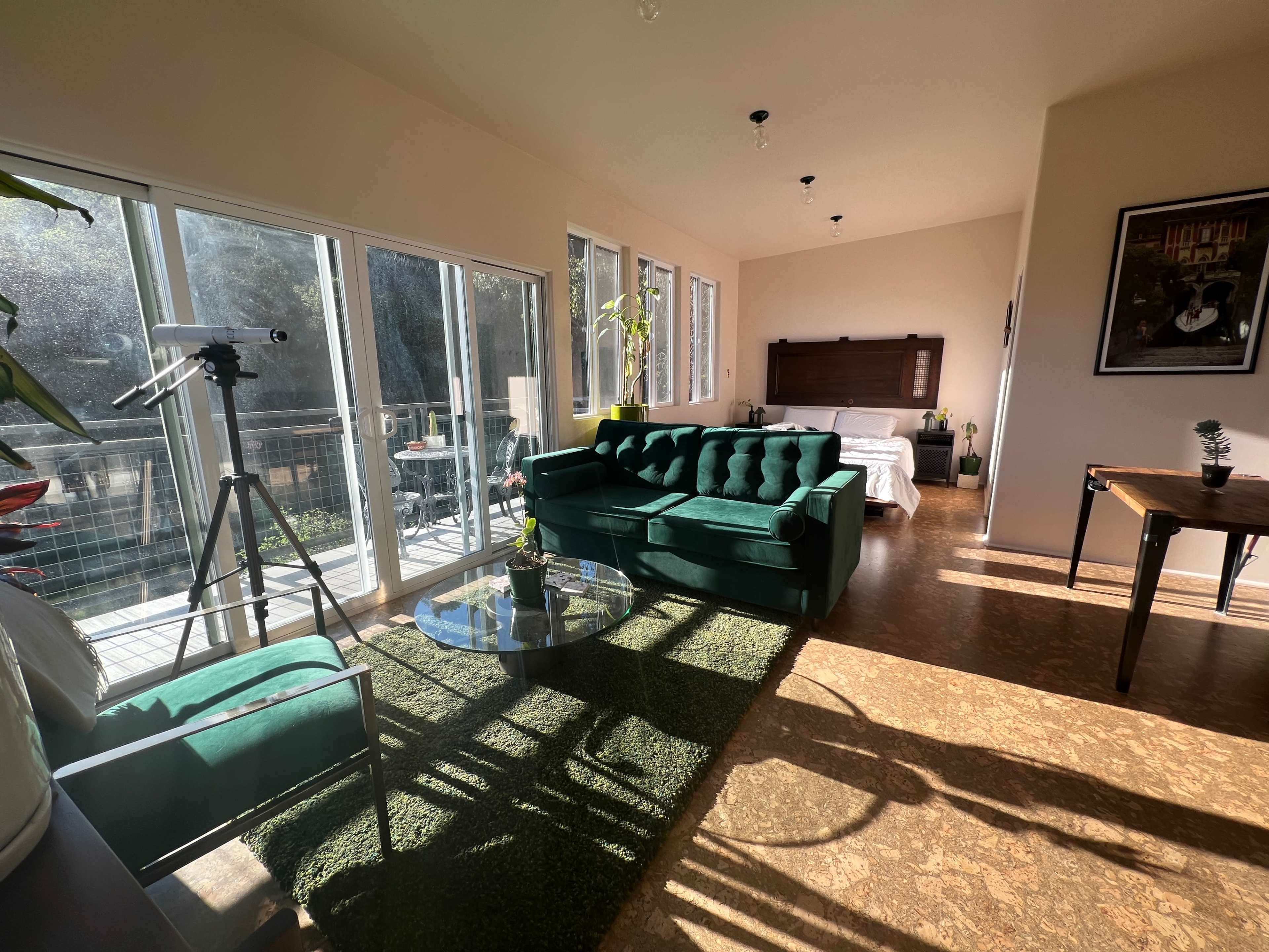 The interior features a green velvet sofa, a glass coffee table, and large windows that flood the space with natural light.