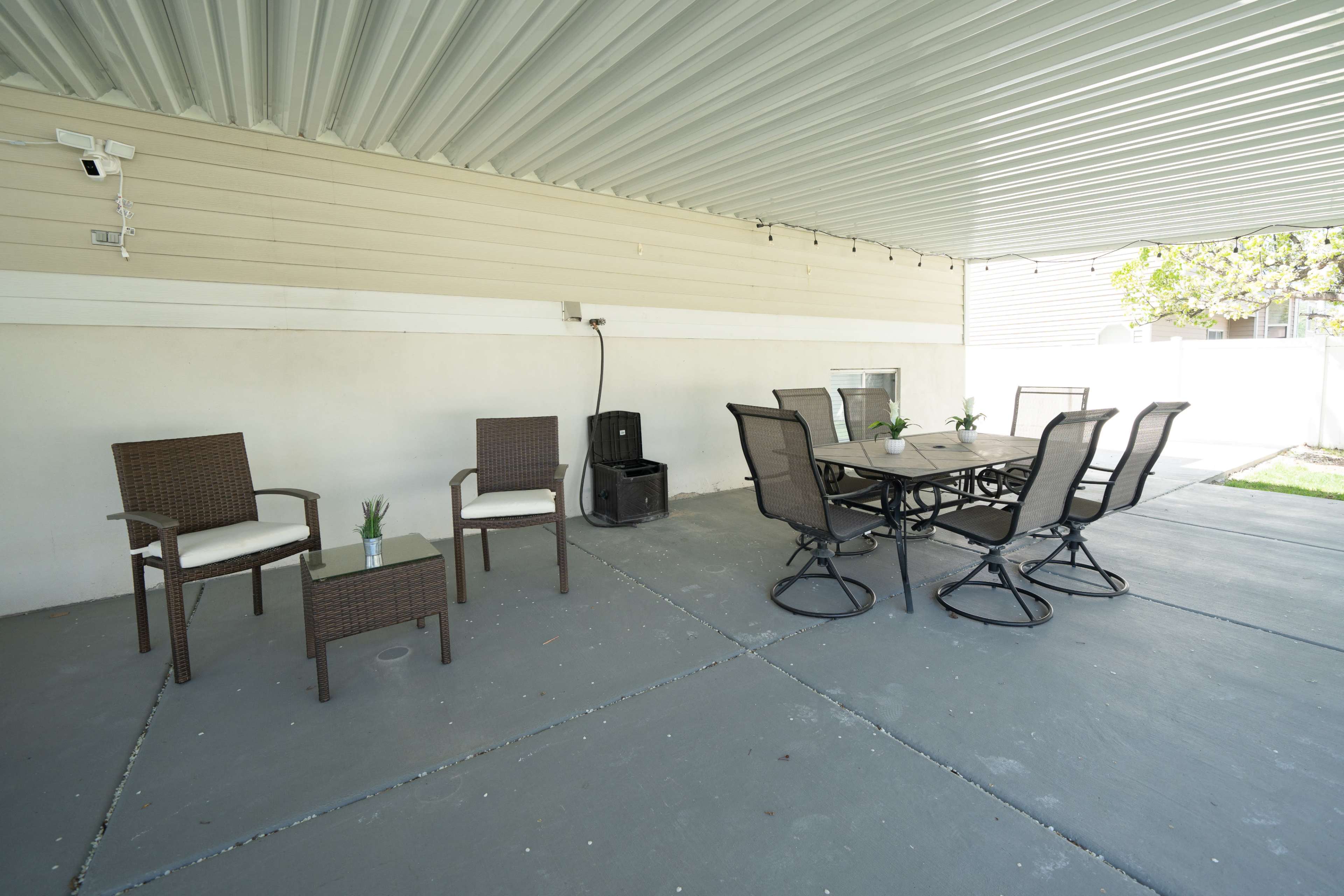 A covered patio area with a table and six chairs, along with two additional chairs on one side.
