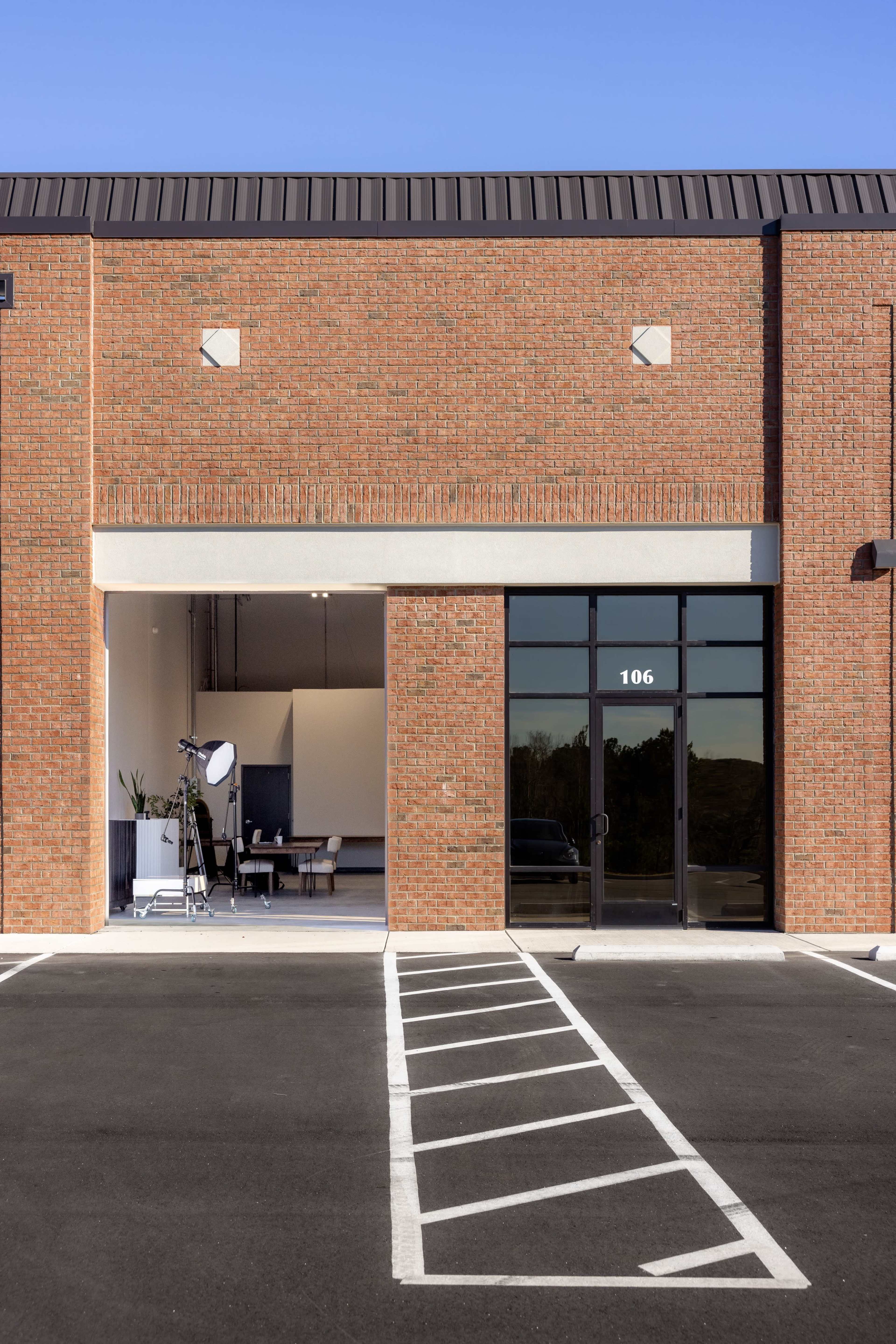A brick commercial building with a large glass door labeled "106" and a parking lot featuring a marked space in front.