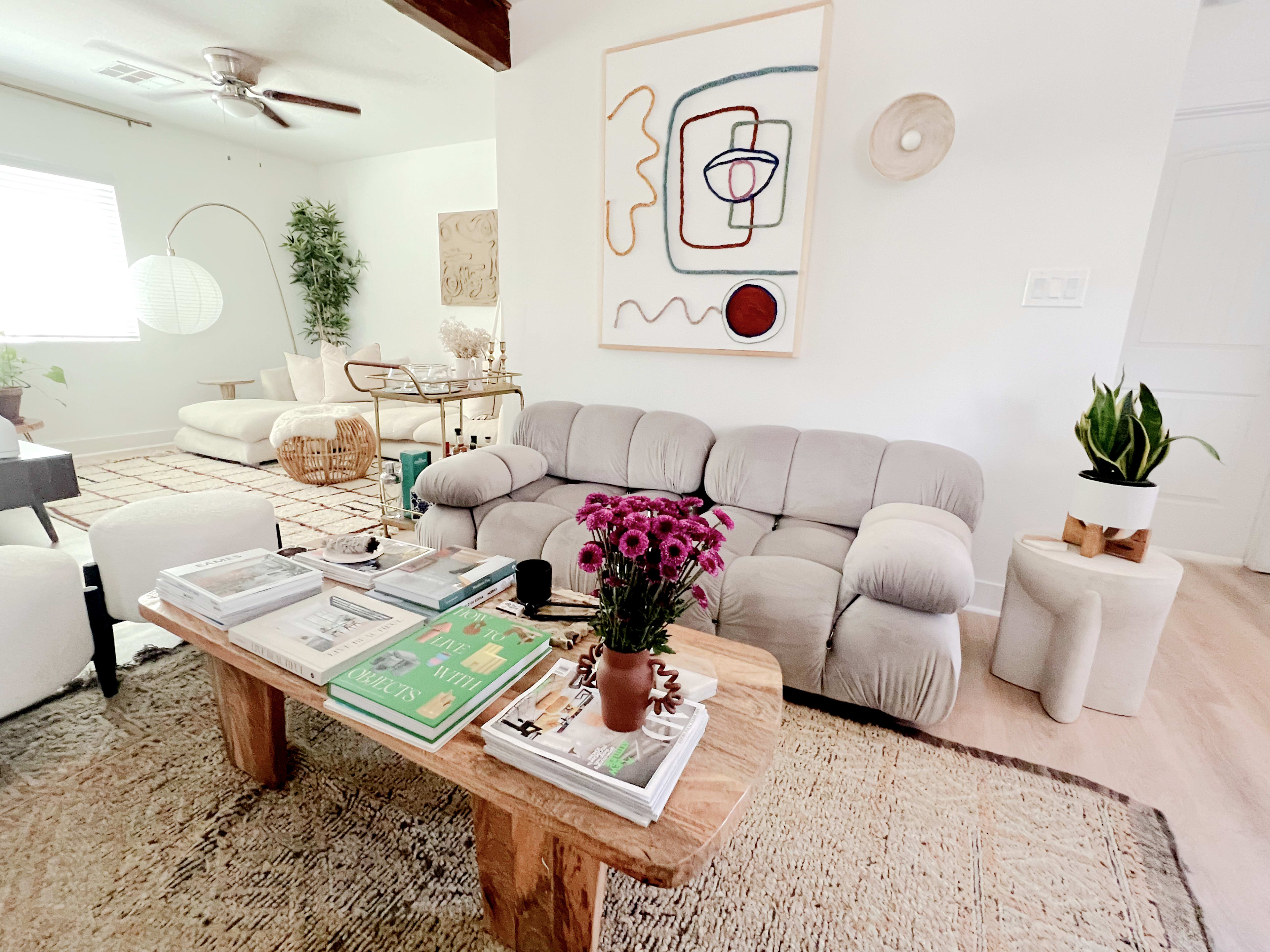 A cozy living room with a gray couch, a wooden coffee table adorned with books and flowers, and an abstract wall art piece.