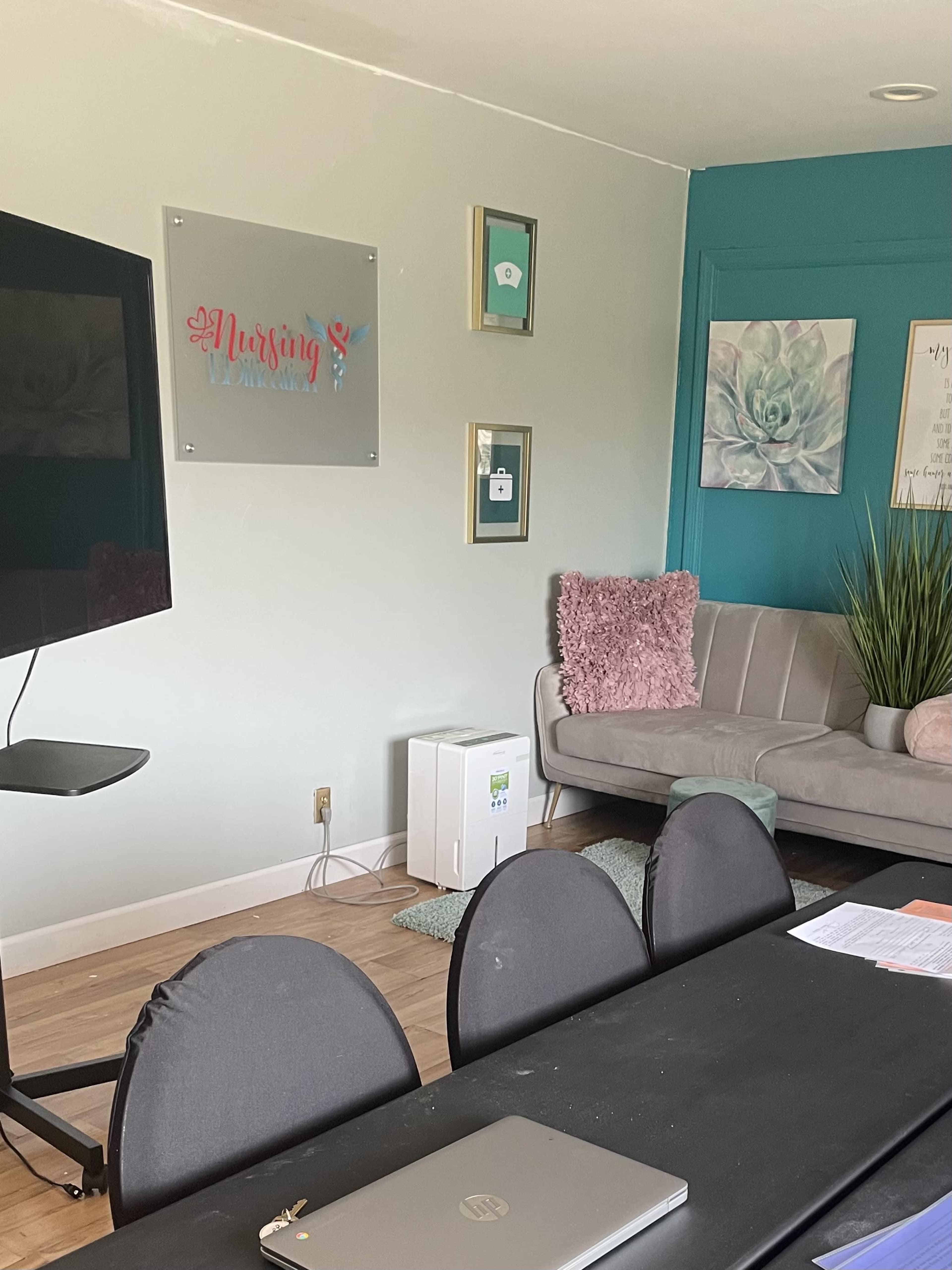 A cozy room with a television, a modern couch, decorative wall art, and a long table with a laptop on it.