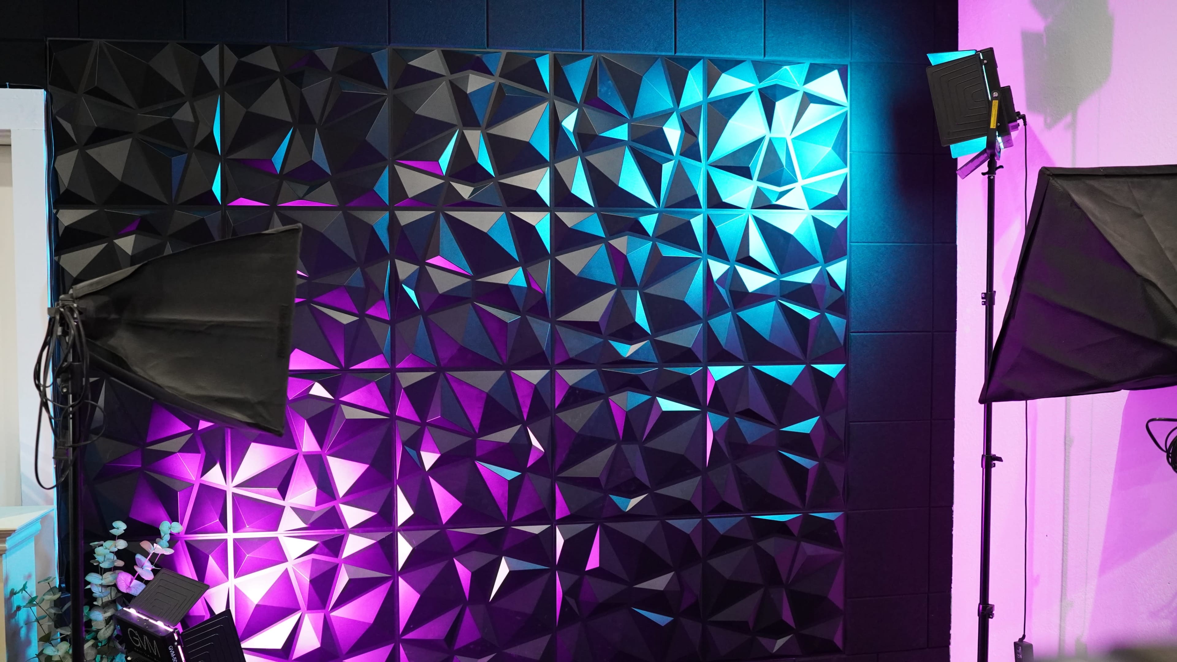 A textured wall with angular, geometric shapes illuminated by colorful lighting from two studio lights.