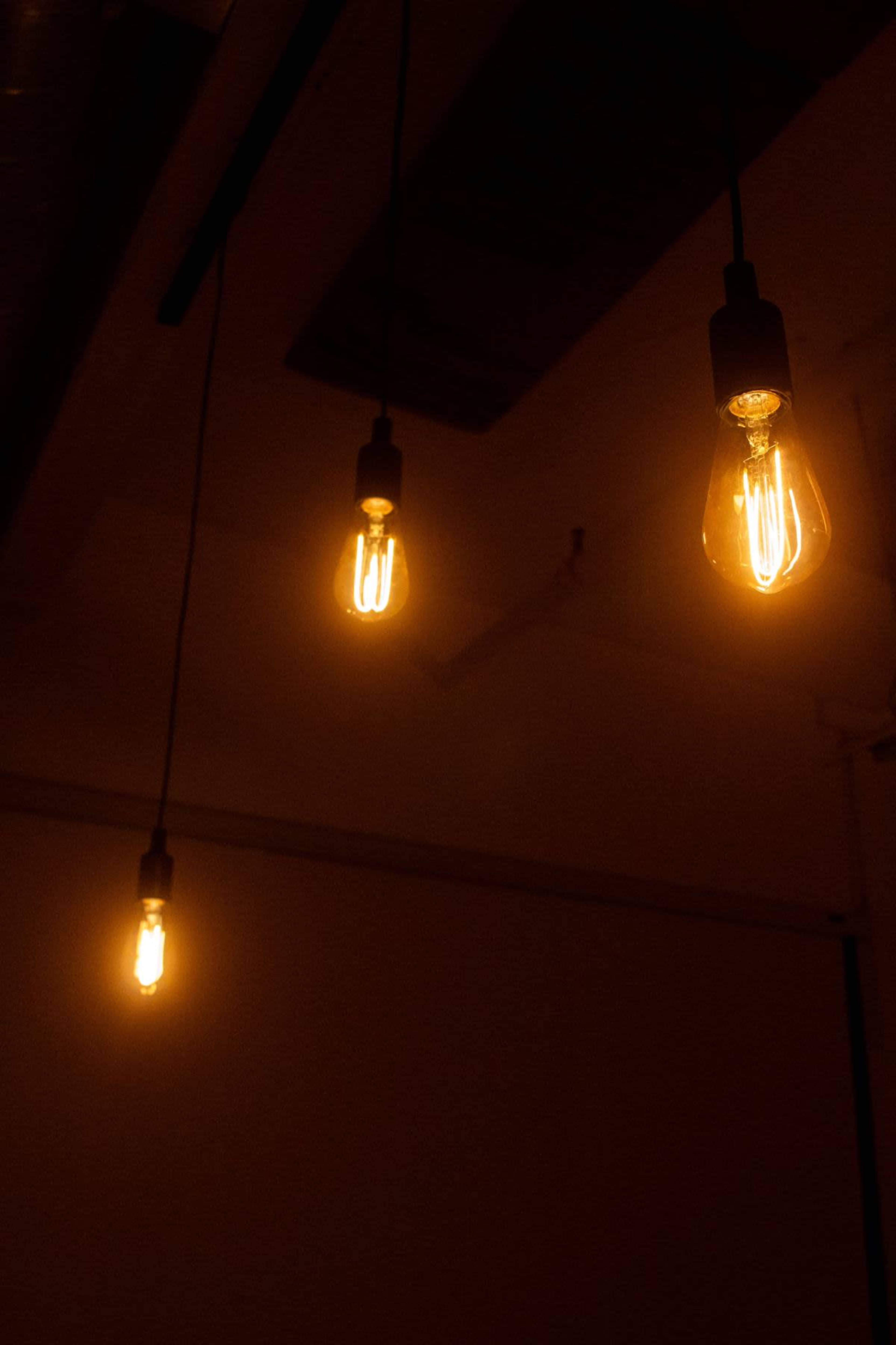 The image shows three vintage-style light bulbs hanging from the ceiling in a dimly lit room.