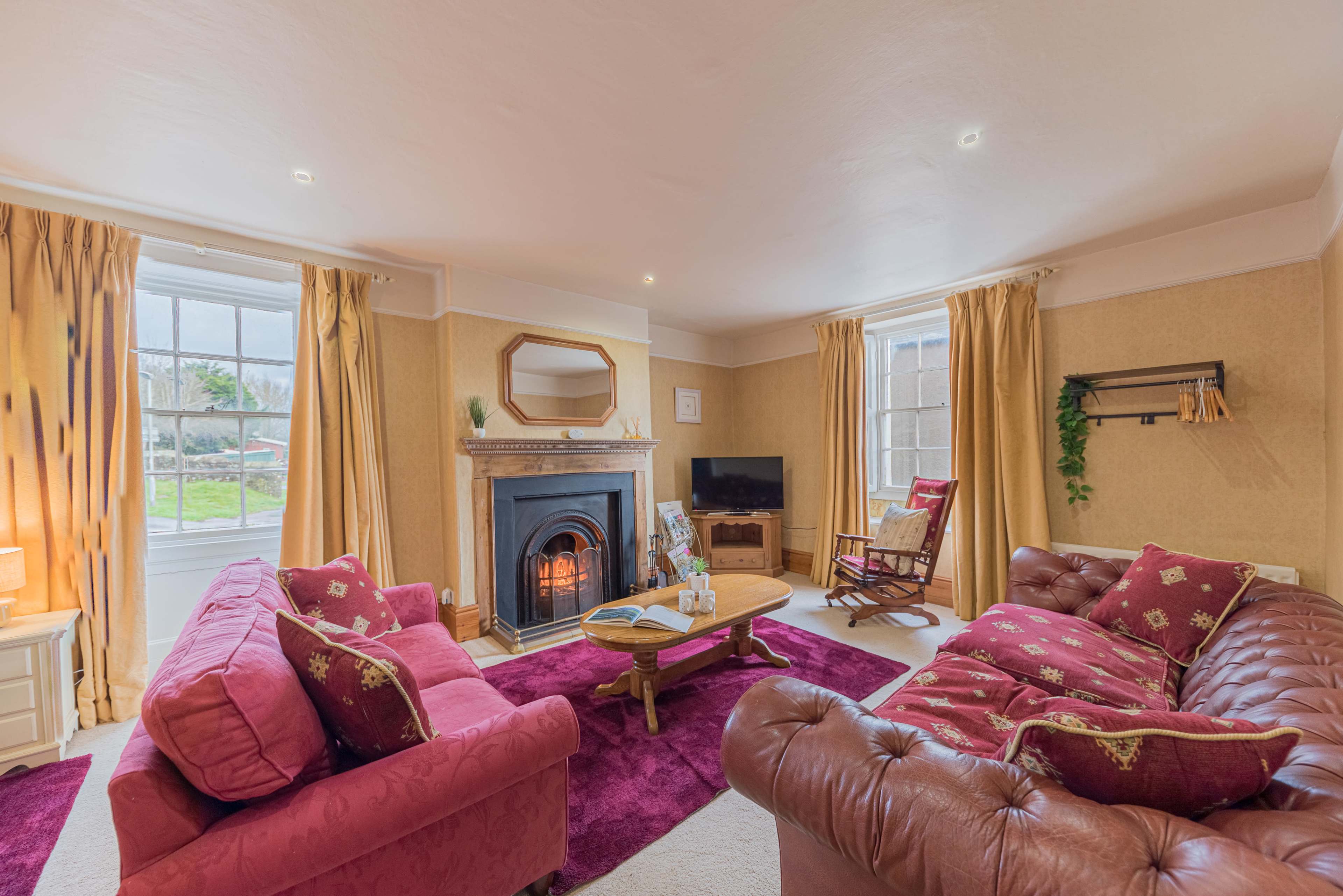 A cozy living room with two upholstered sofas, a fireplace, a television, and large windows that let in natural light.