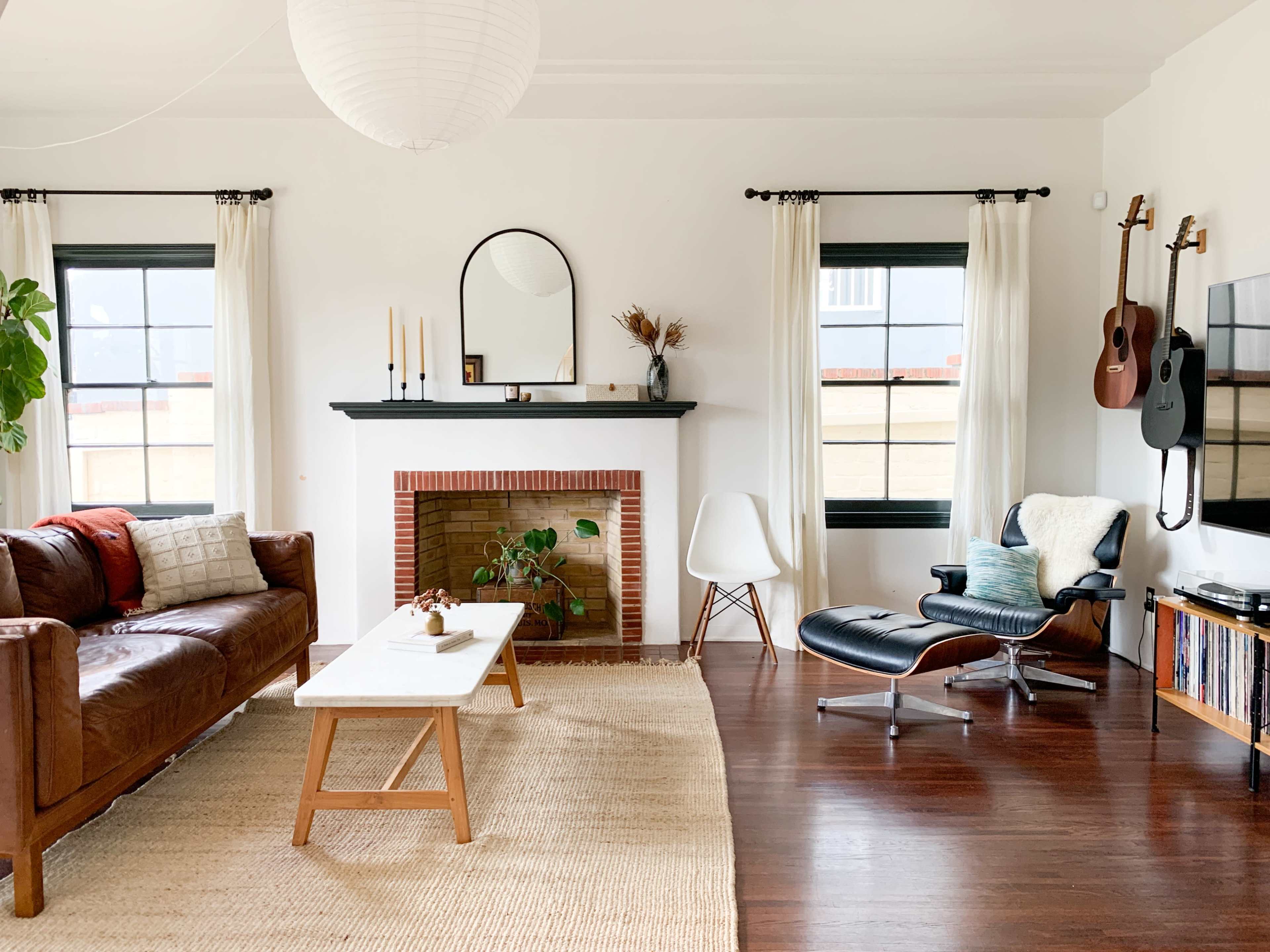 A cozy living room features a brown leather couch, a white coffee table, a fireplace with candles, and a guitar hanging on the wall.