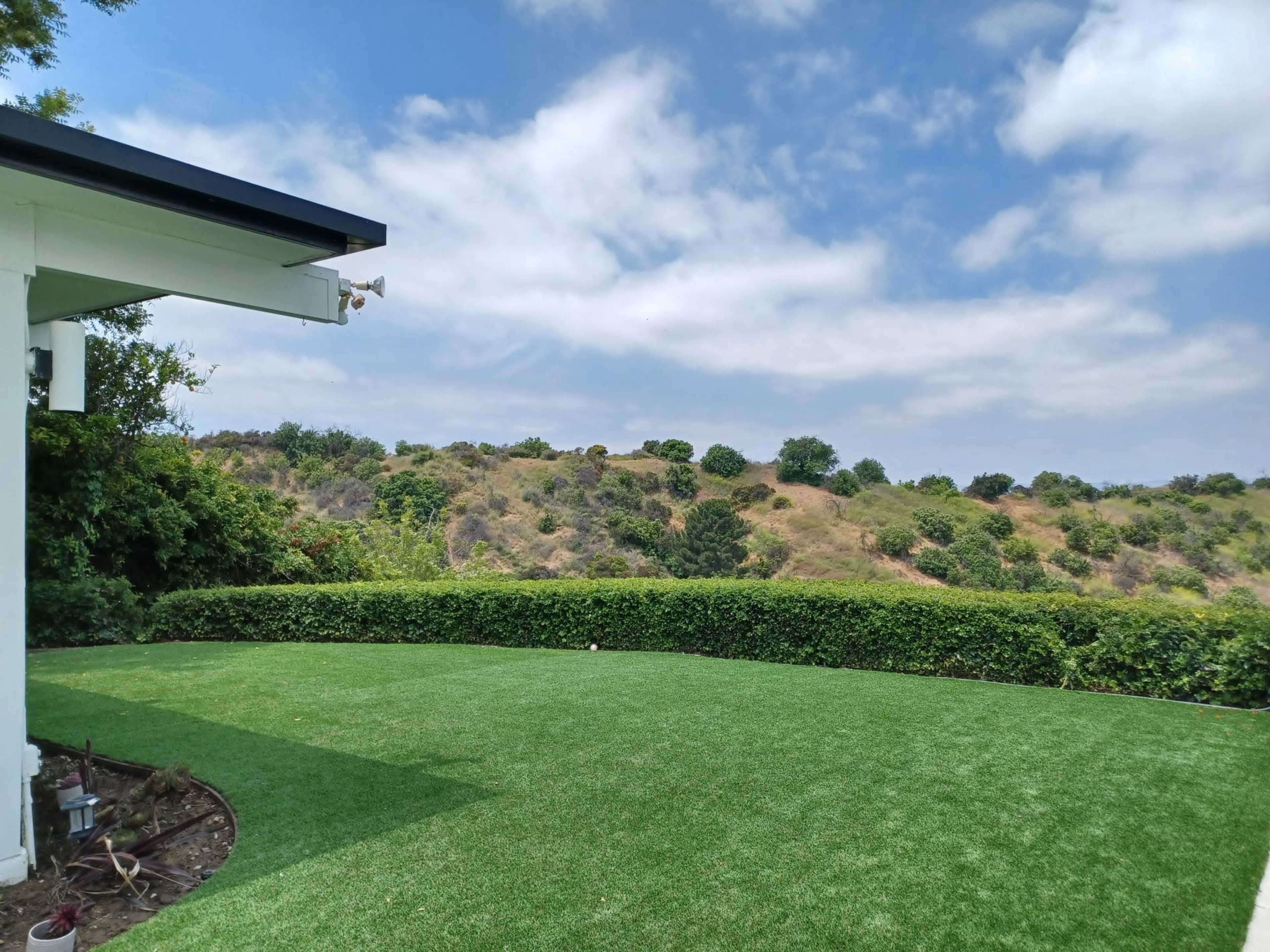 The image shows a green lawn with a hedge and rolling hills under a partly cloudy sky.