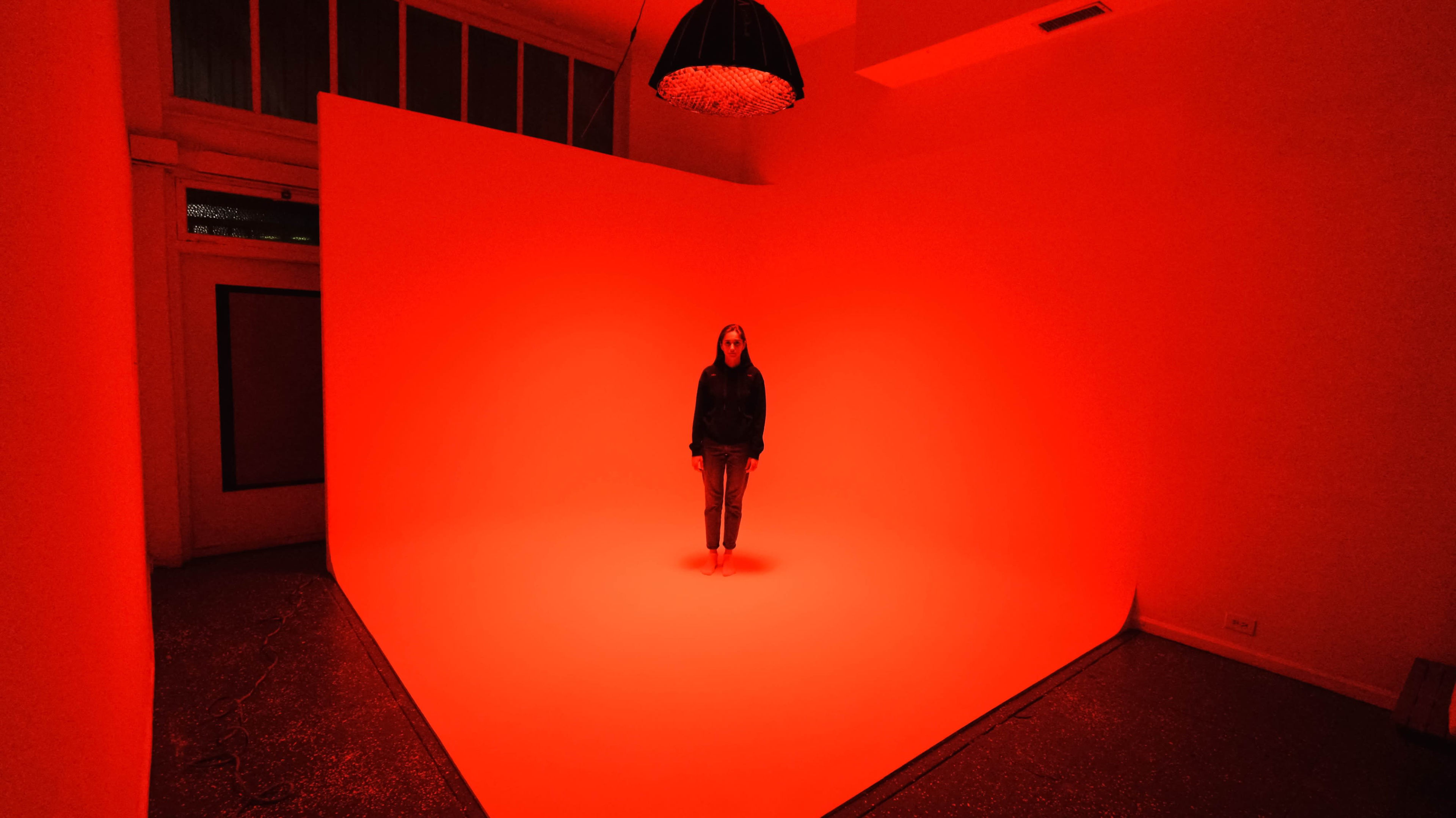A person stands alone in a room with red lighting and a large red backdrop.