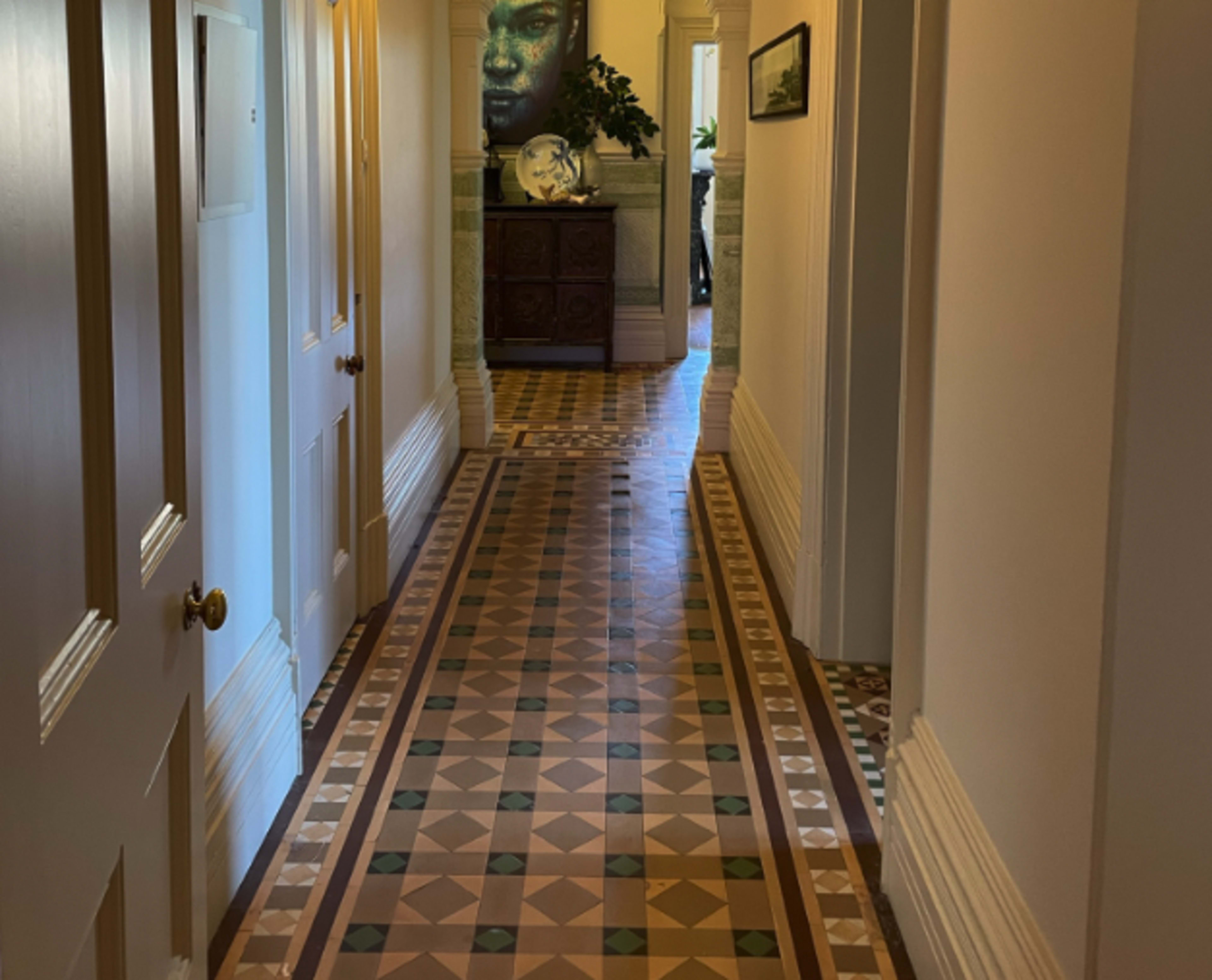 A long corridor with patterned tiled flooring, flanked by doors on one side and a large piece of artwork at the far end.
