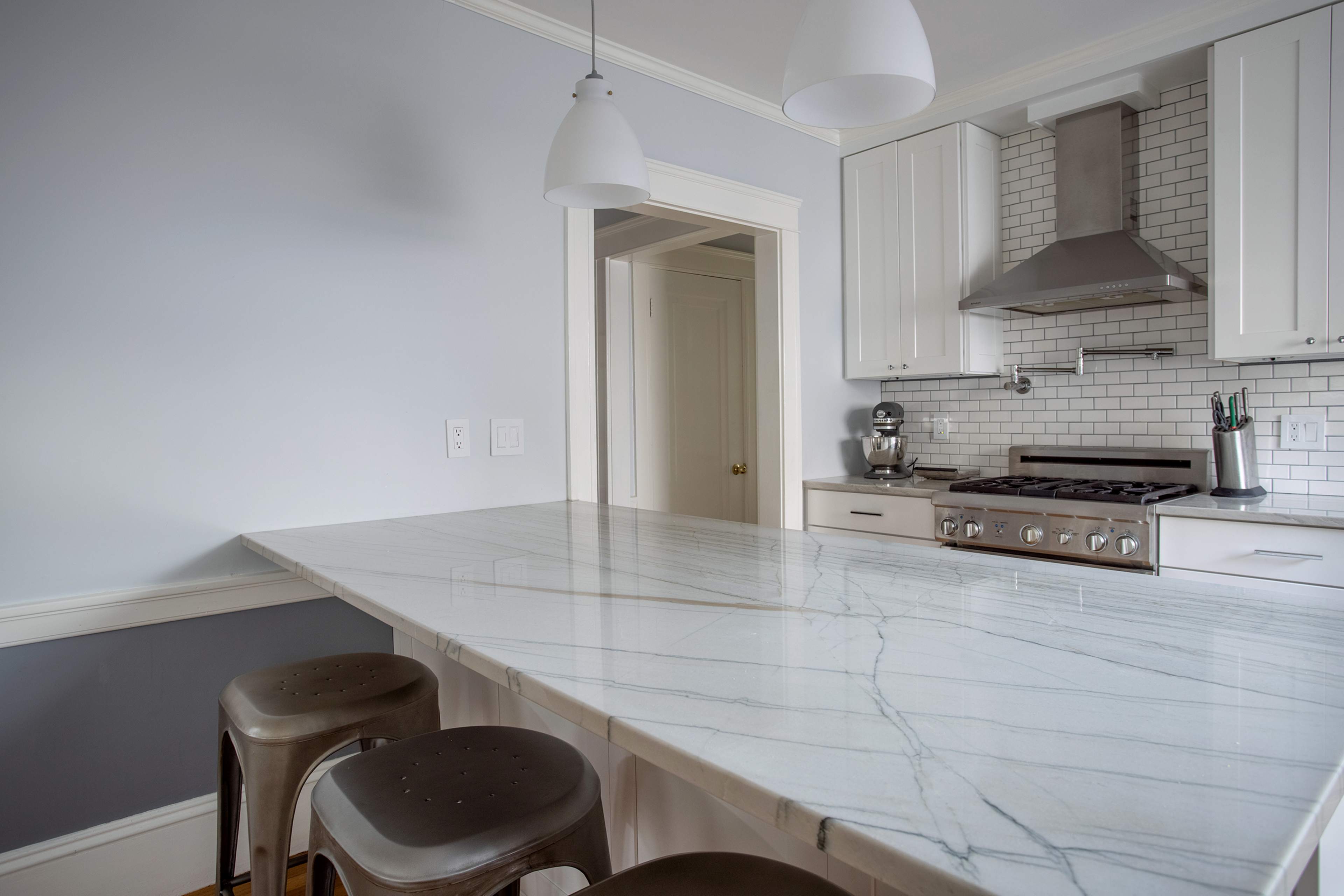 A modern kitchen features a marble countertop with gray veining, stainless steel appliances, and minimalist white cabinetry.