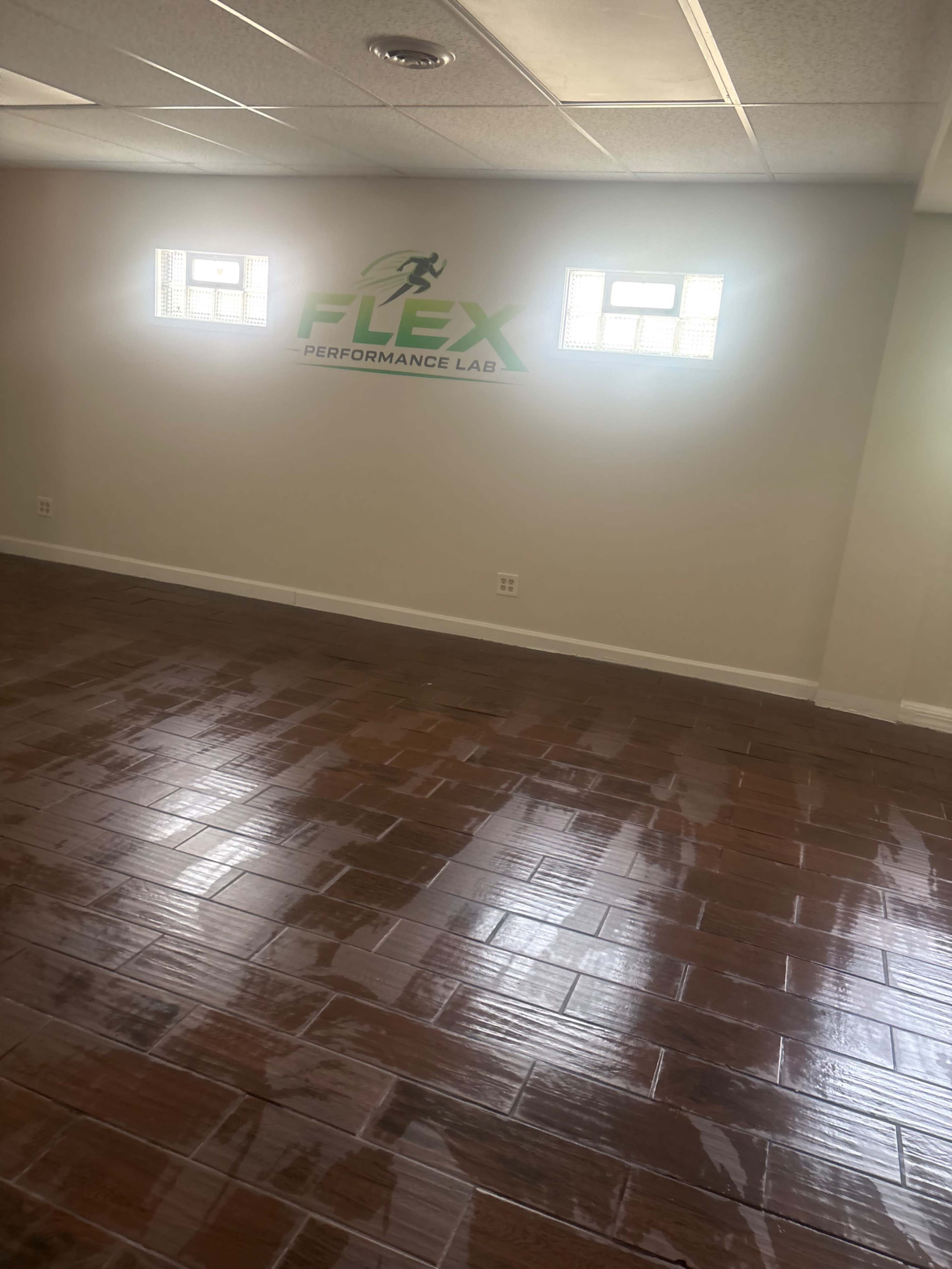 A clean, vacant room with hardwood flooring and a wall featuring the logo for "FLEX Performance Lab."