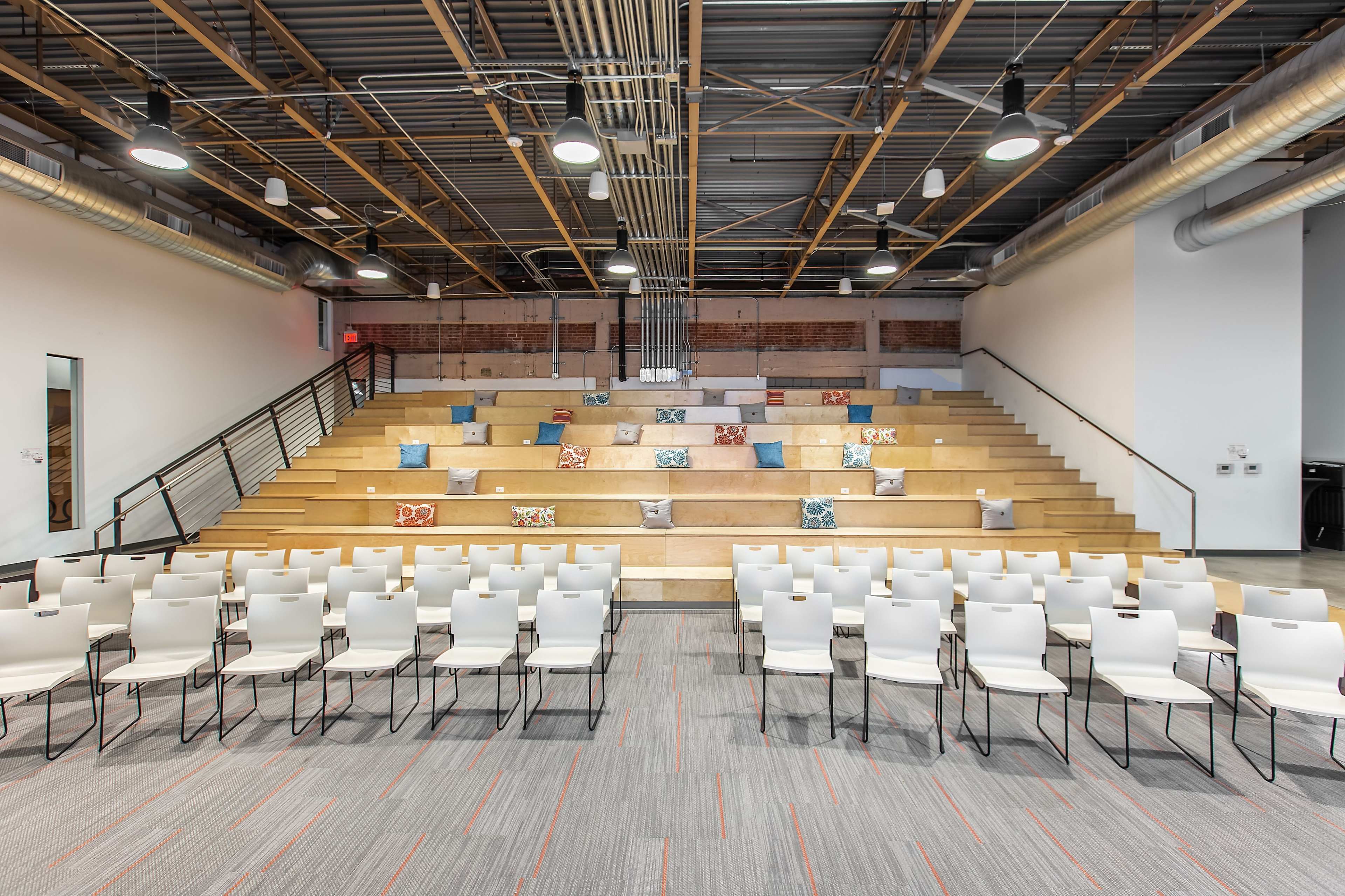A modern auditorium setting with tiered seating, white chairs arranged neatly in rows, and decorative pillows placed on the steps.