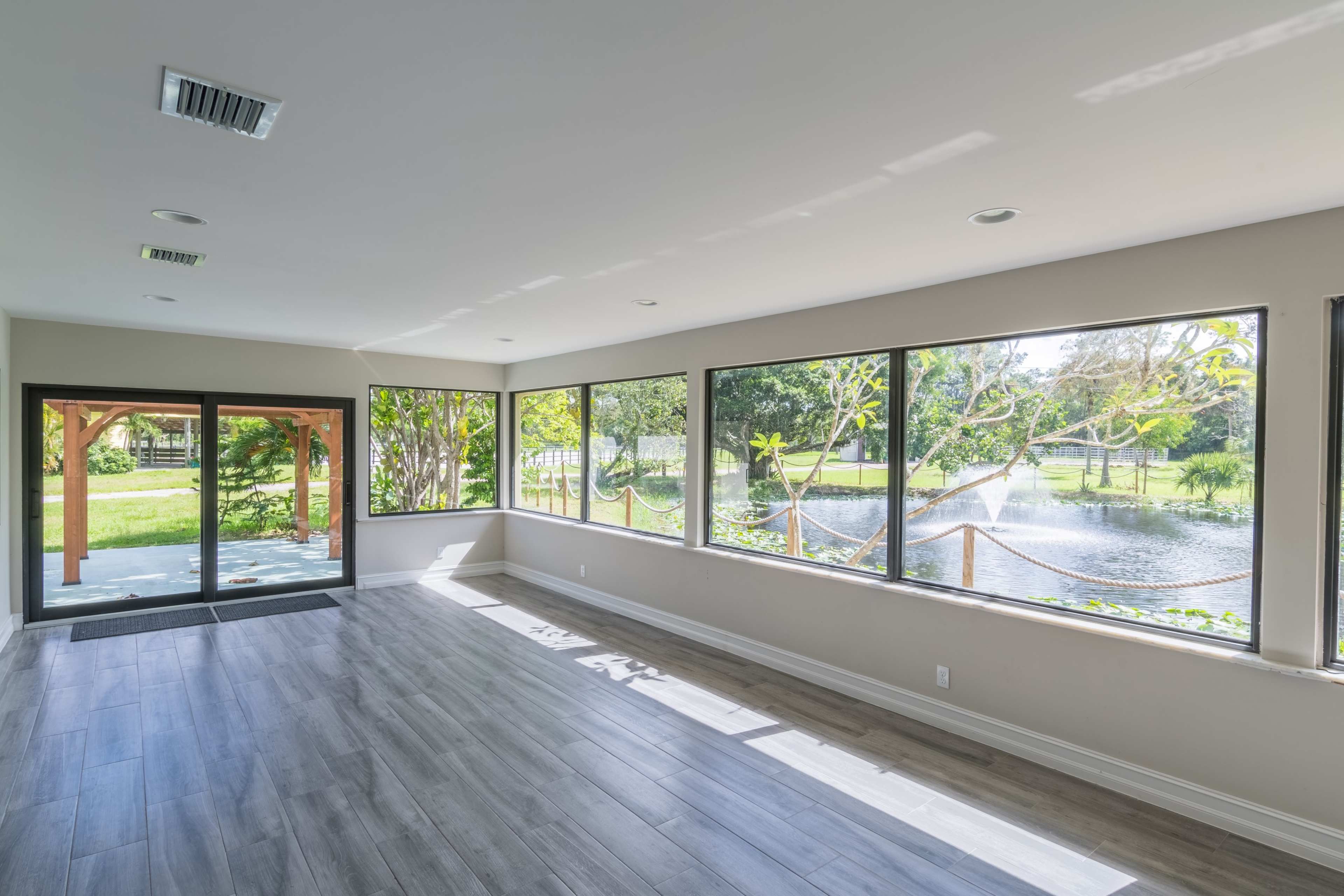 A spacious room features large windows overlooking a serene body of water and lush greenery.