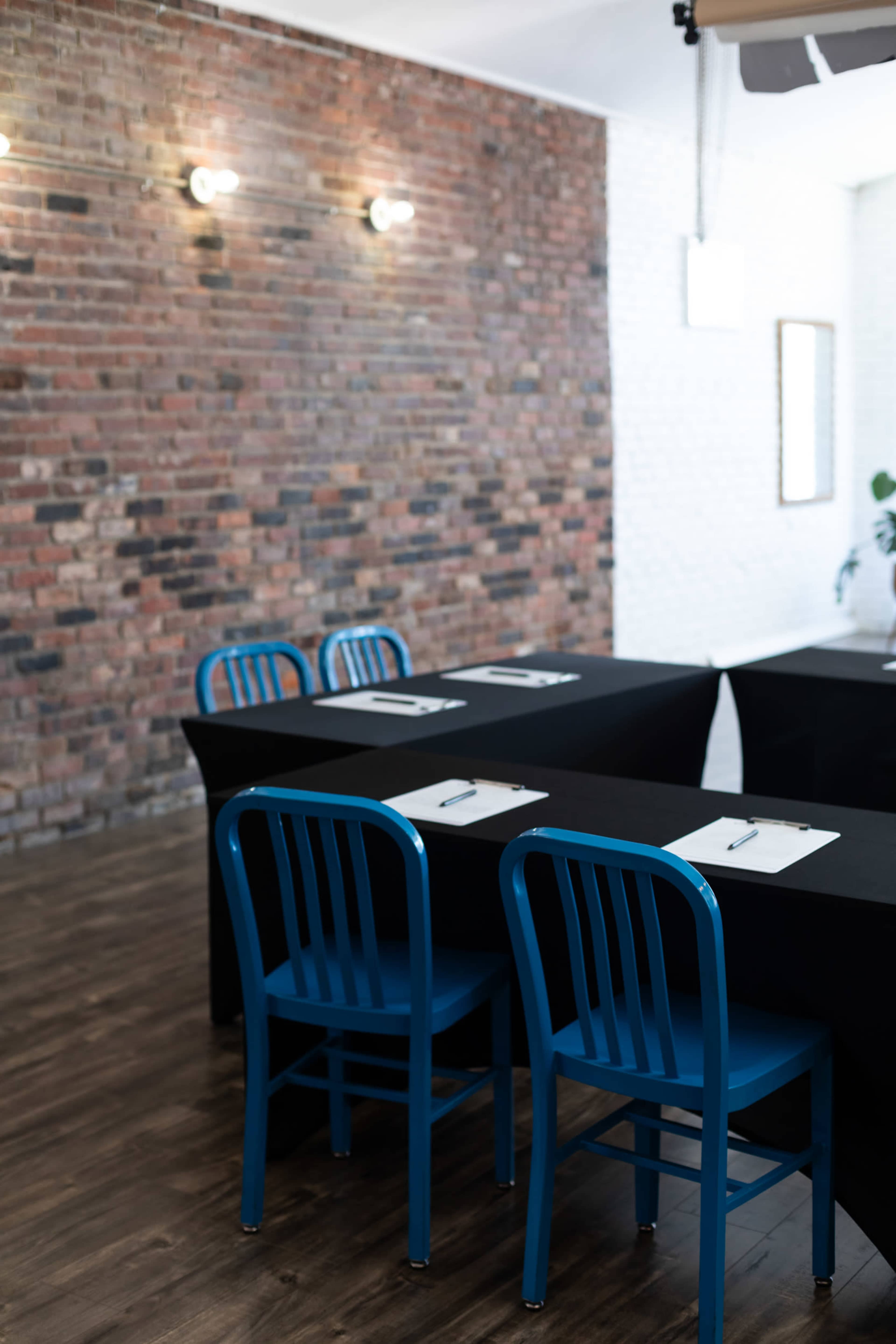A meeting room features a long black table with blue chairs and a brick wall backdrop.