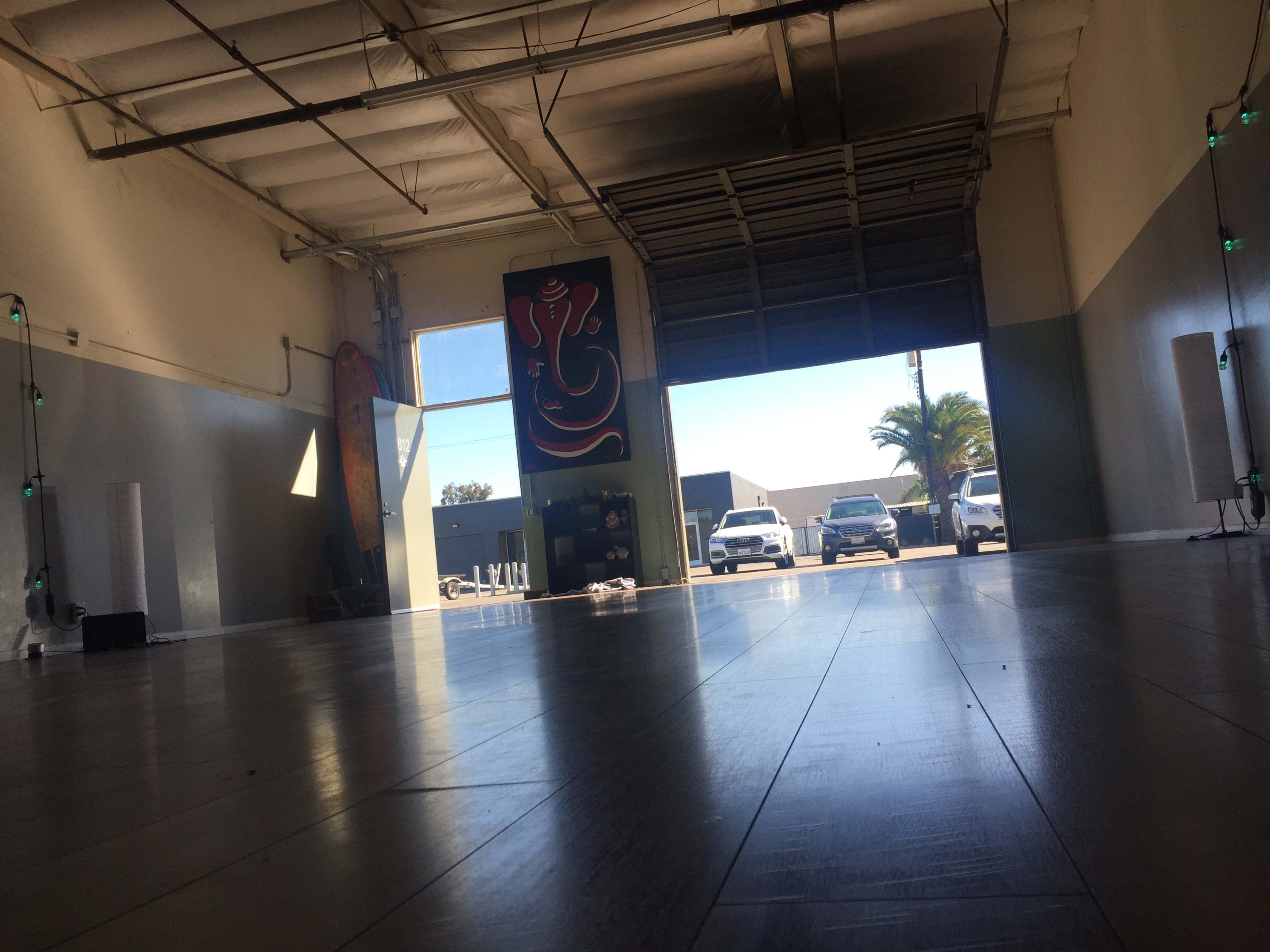 The interior of a spacious industrial room features a large mural and large doors open to a parking area with several vehicles.