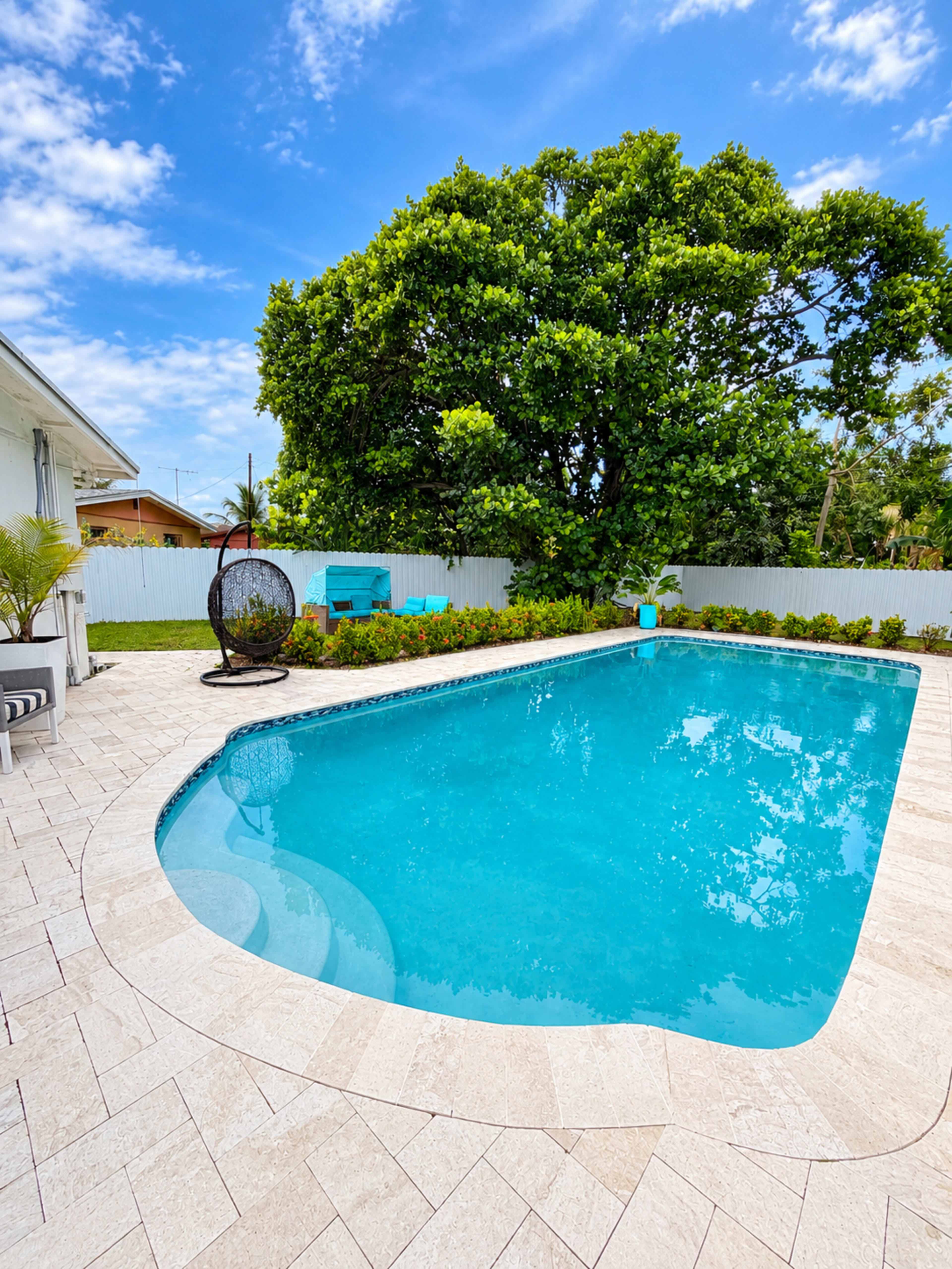 A crystal-clear swimming pool is surrounded by a landscaped area with a large tree and seating arrangements.