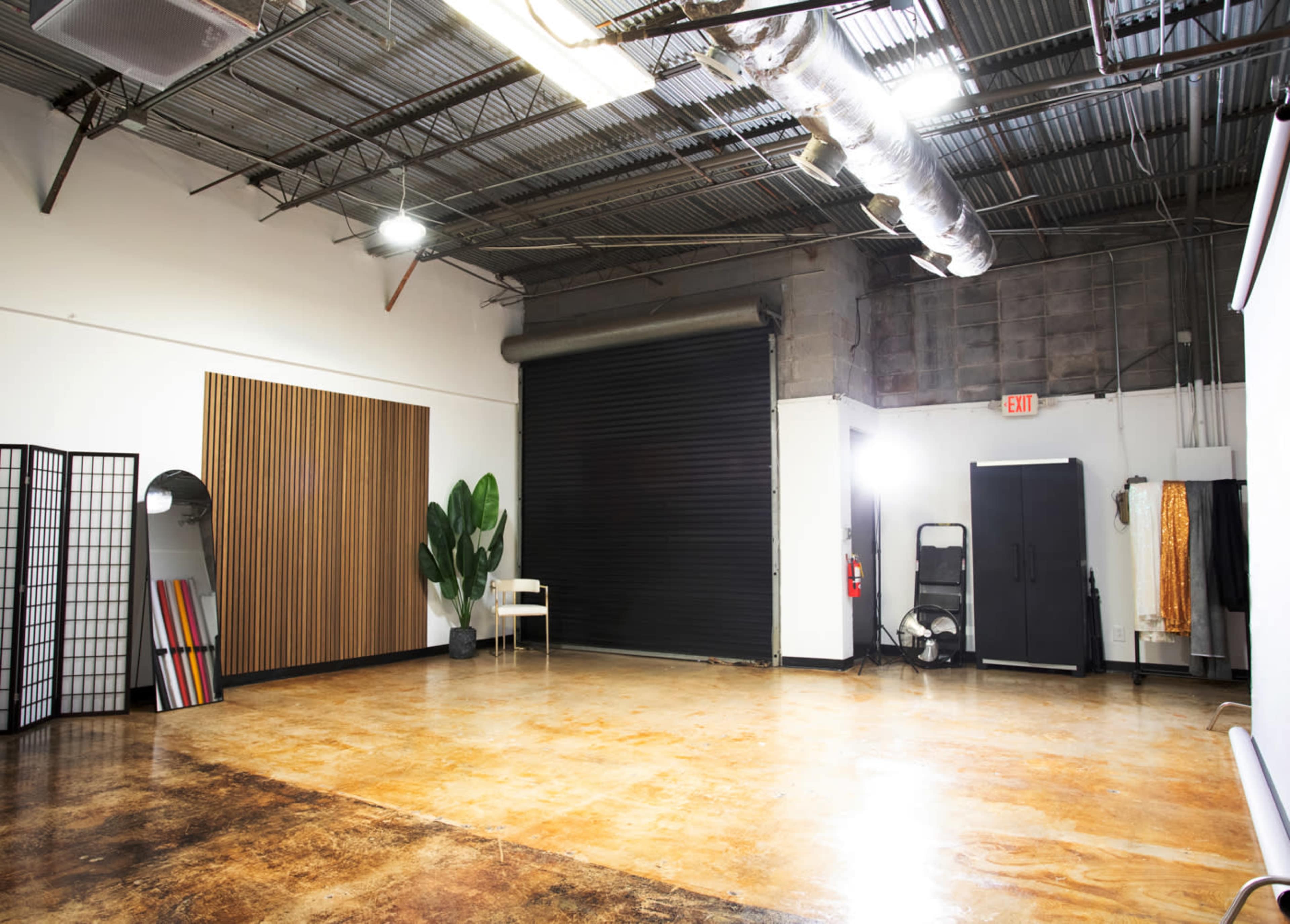 The image shows a spacious, industrial-style room with a polished concrete floor, black roll-up door, and minimalist furnishings.