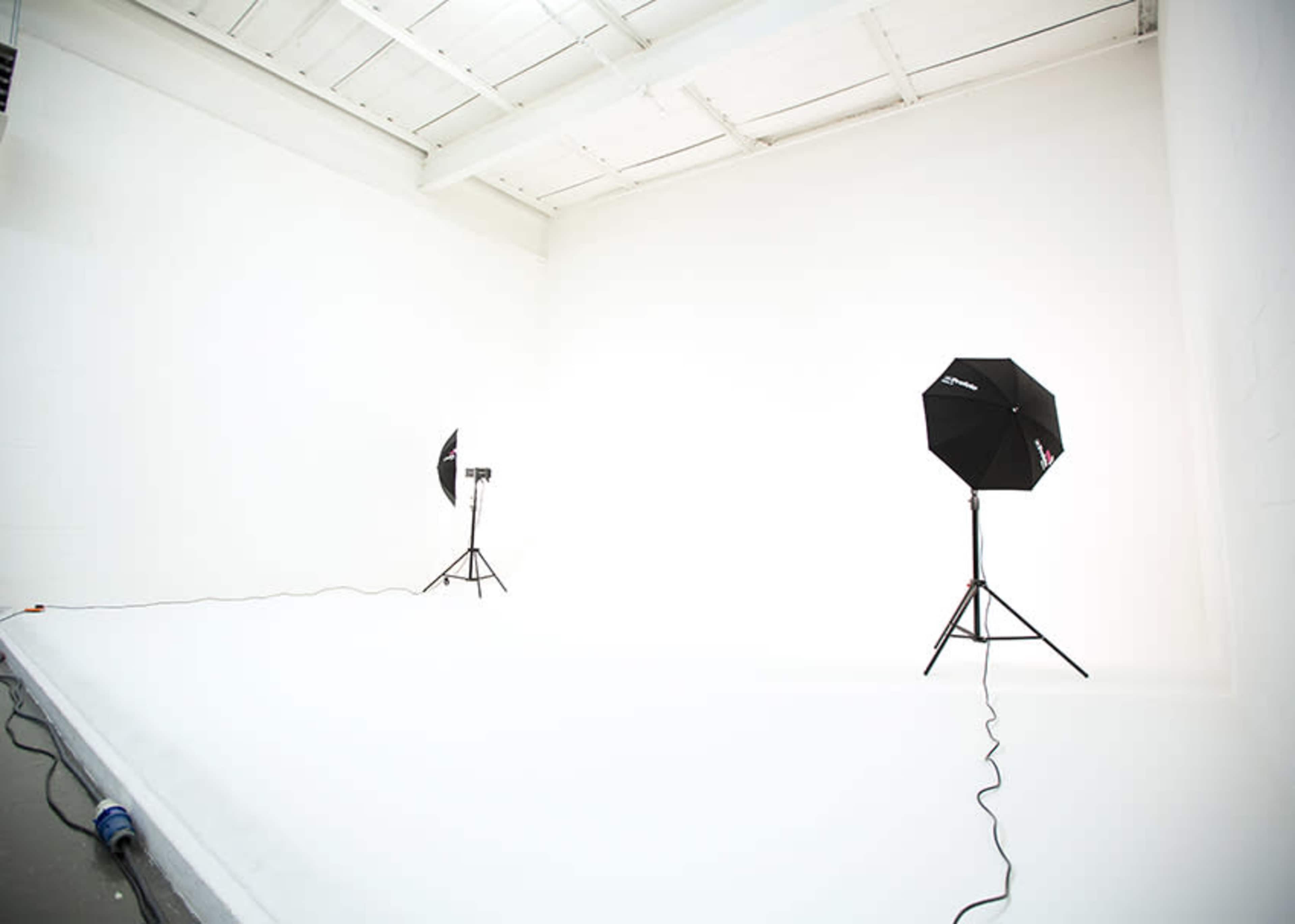 An empty photography studio with two light stands and a seamless white backdrop.