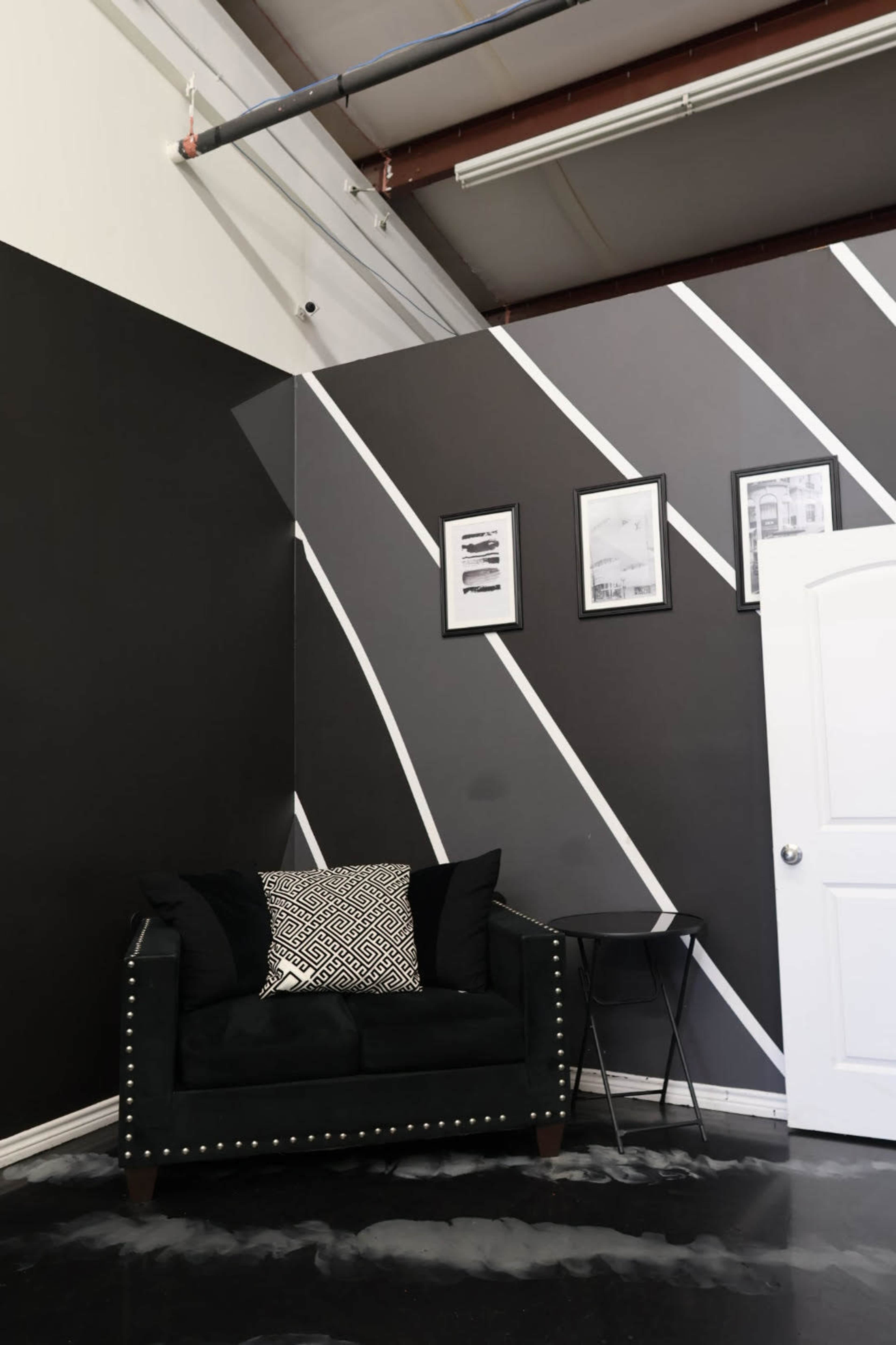 The image shows a modern interior space featuring a black couch with decorative pillows, a small side table, and black and white striped wall art.