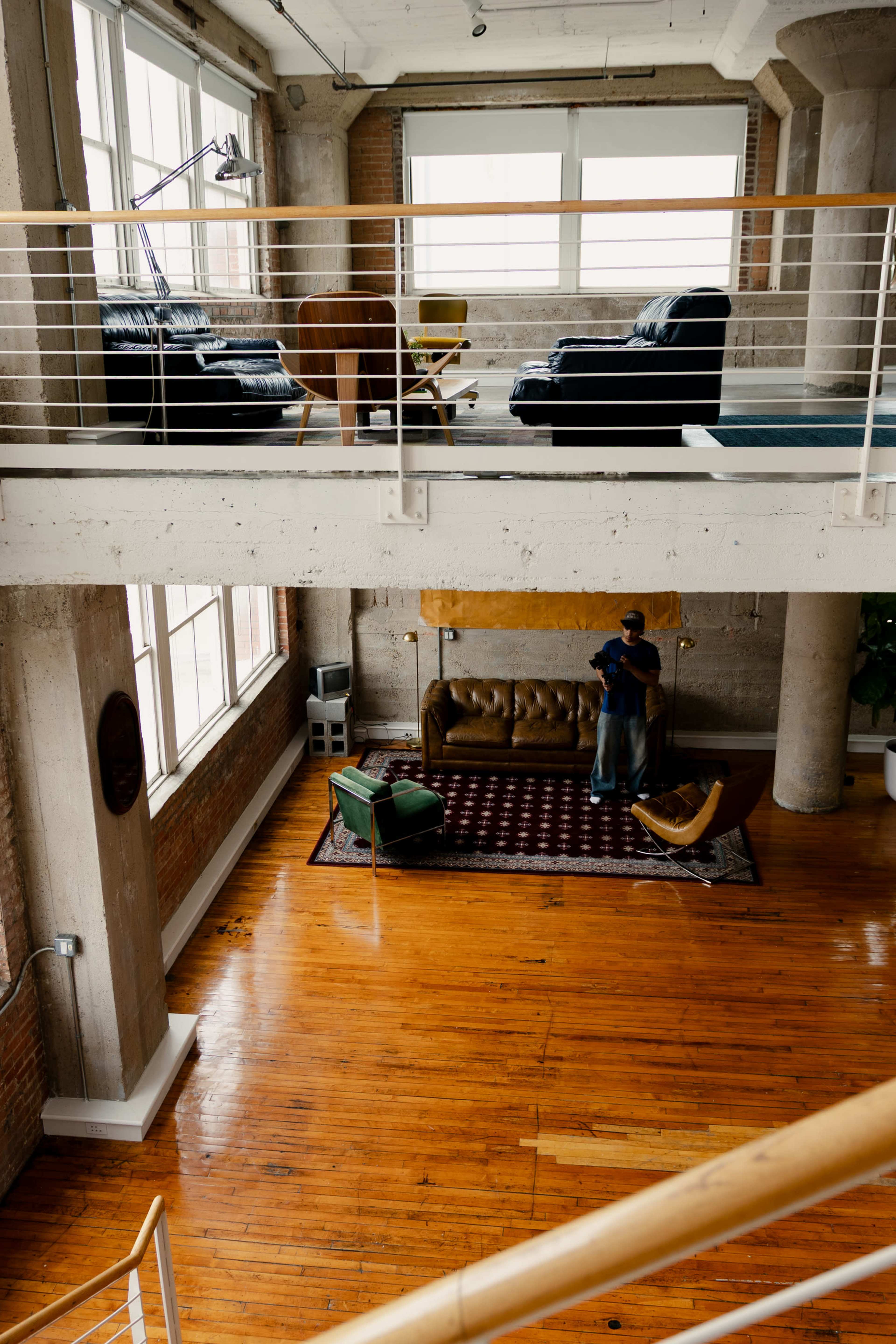 The image shows a spacious, modern living area divided across two levels, featuring a mix of seating options and large windows that provide natural light.