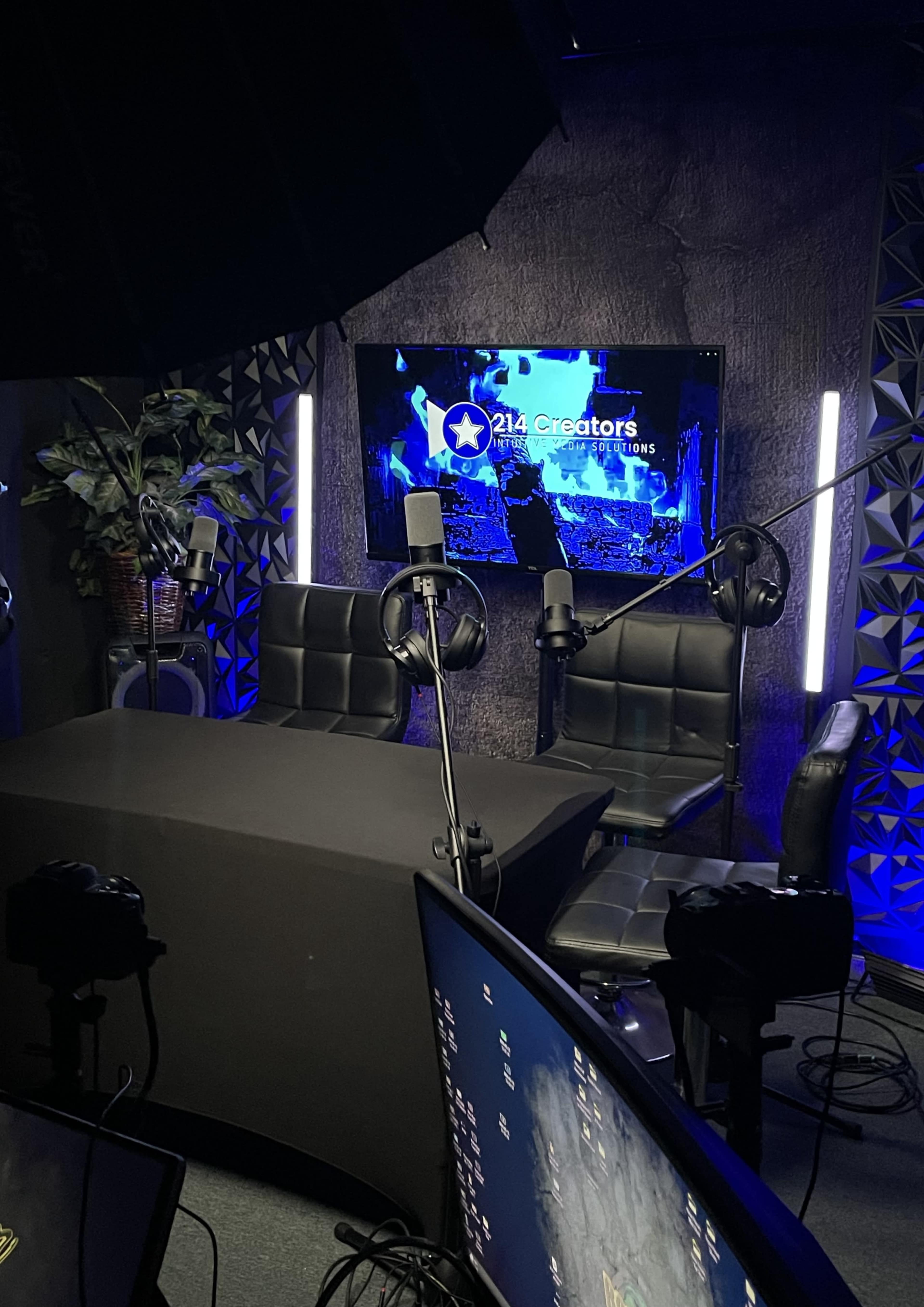 A podcast studio features a dark table with two black chairs, microphones, and a backdrop displaying "214 Creators."