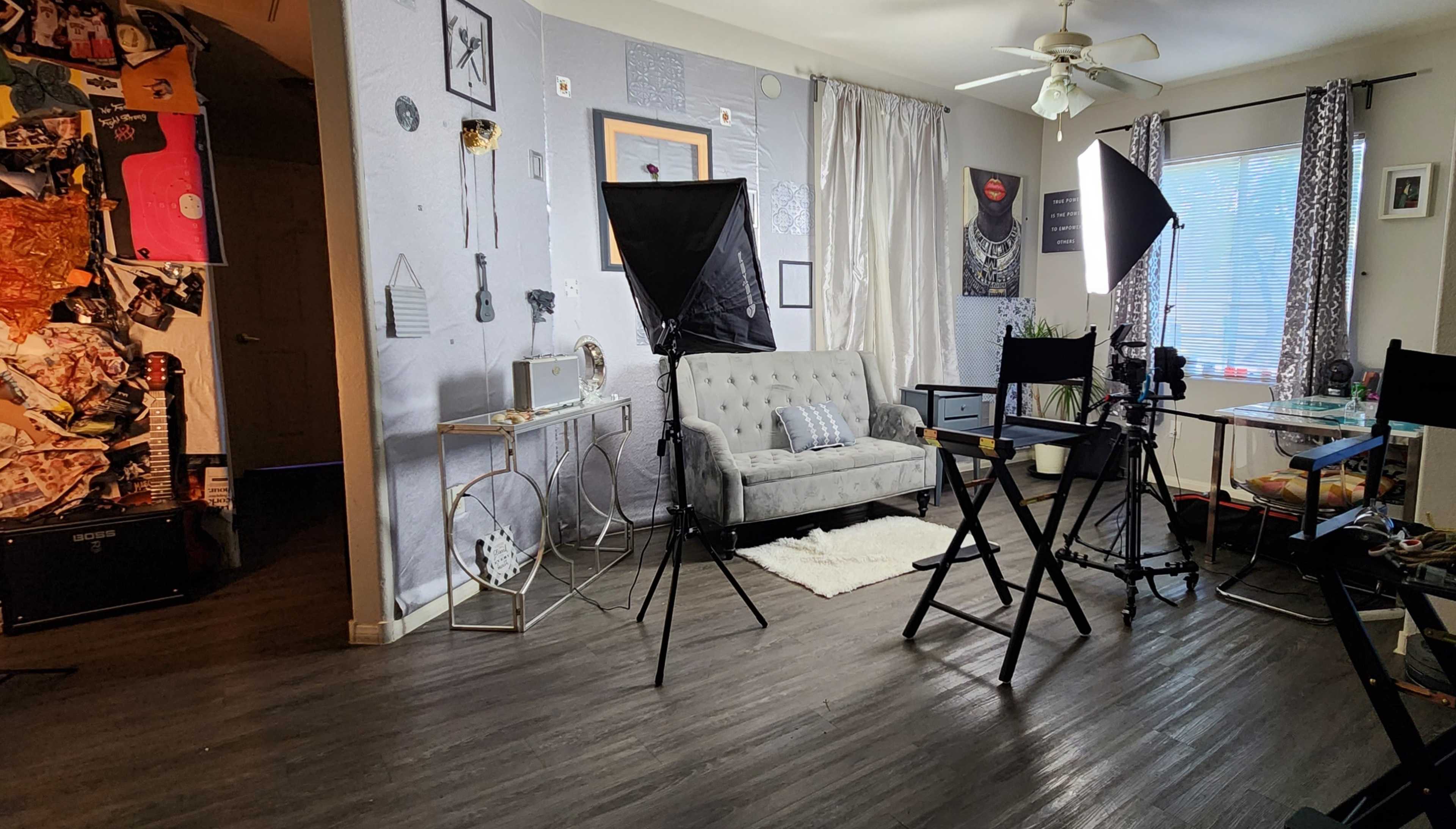 A small living room setup with a gray couch, studio lighting equipment, and a table, all arranged for a photo or video shoot.
