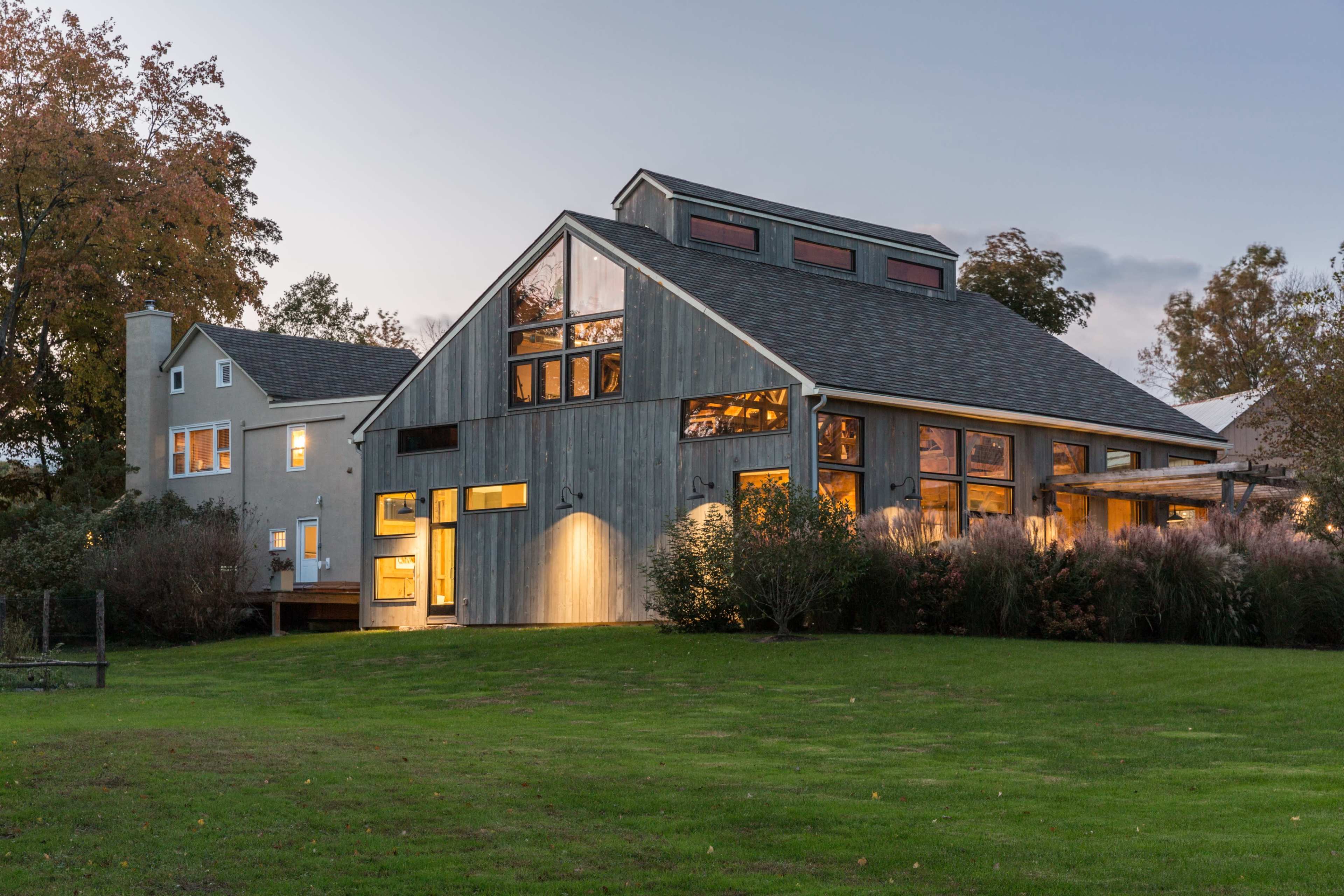 A modern two-story wooden house with large windows, set in a grassy area surrounded by trees.