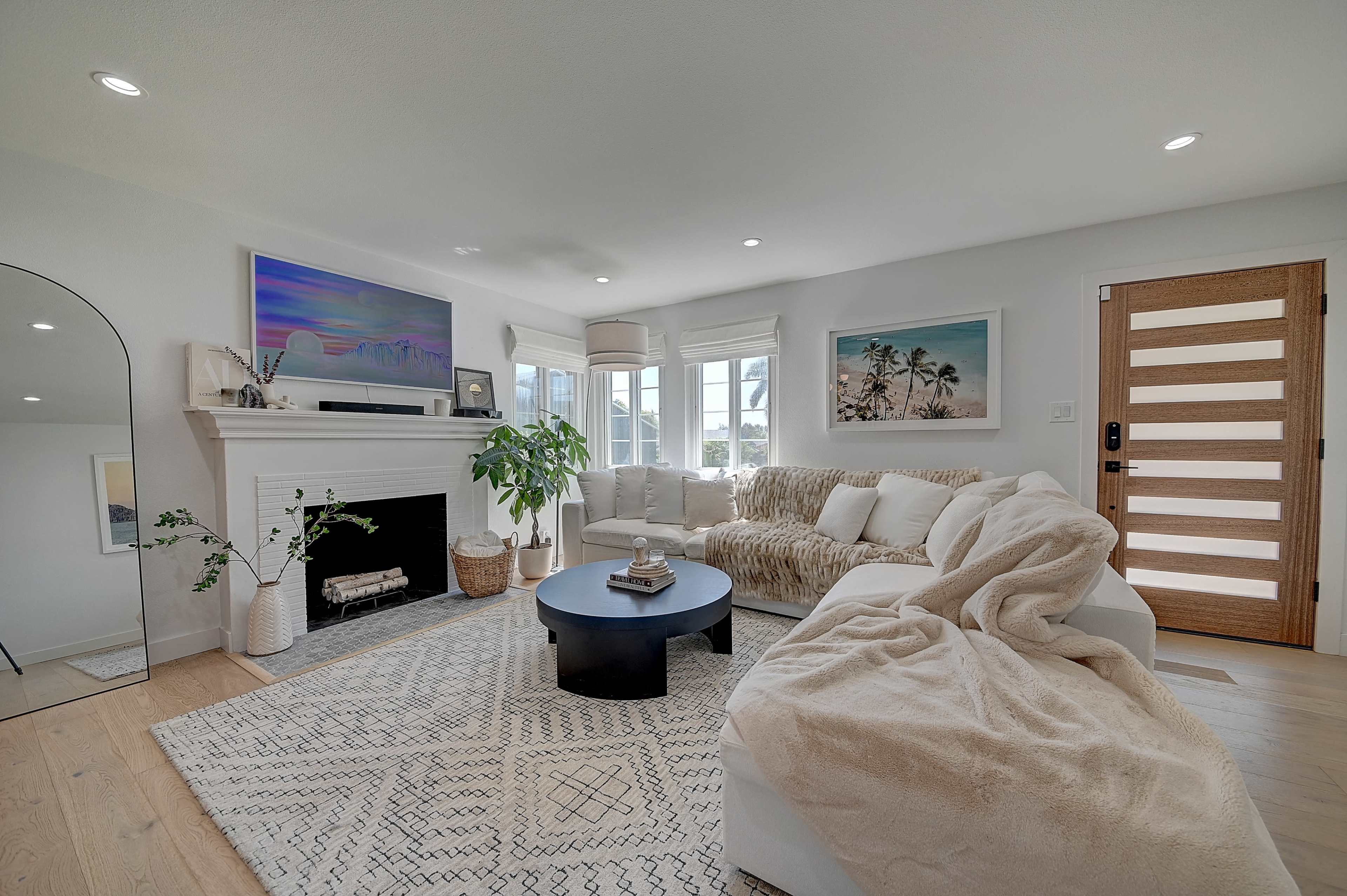 A modern living room with a large sectional sofa, a round coffee table, a fireplace, and large windows allowing natural light.