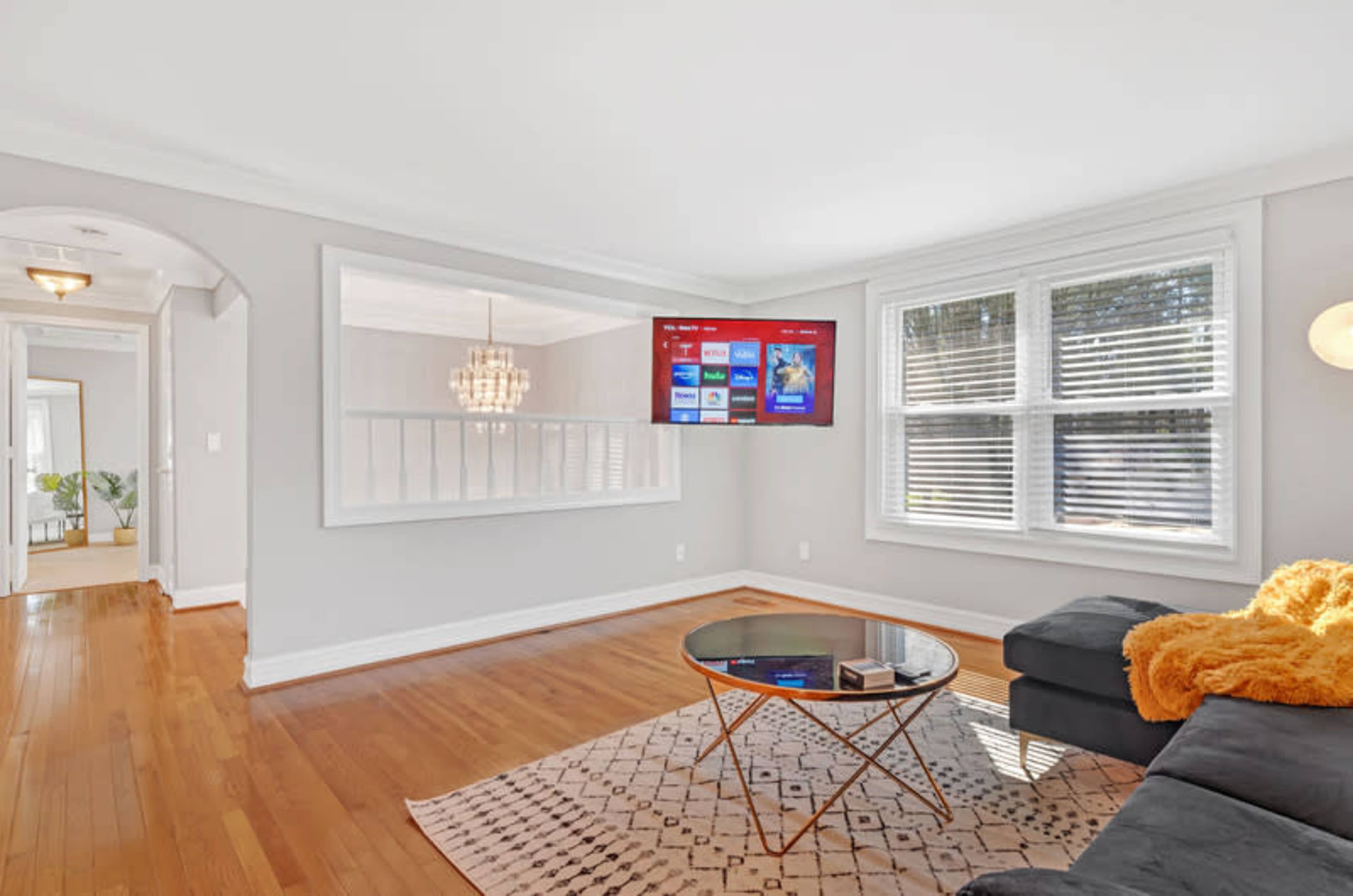 A living room with a dark sectional sofa, a round glass coffee table, and a television mounted on the wall, featuring a streaming service interface.