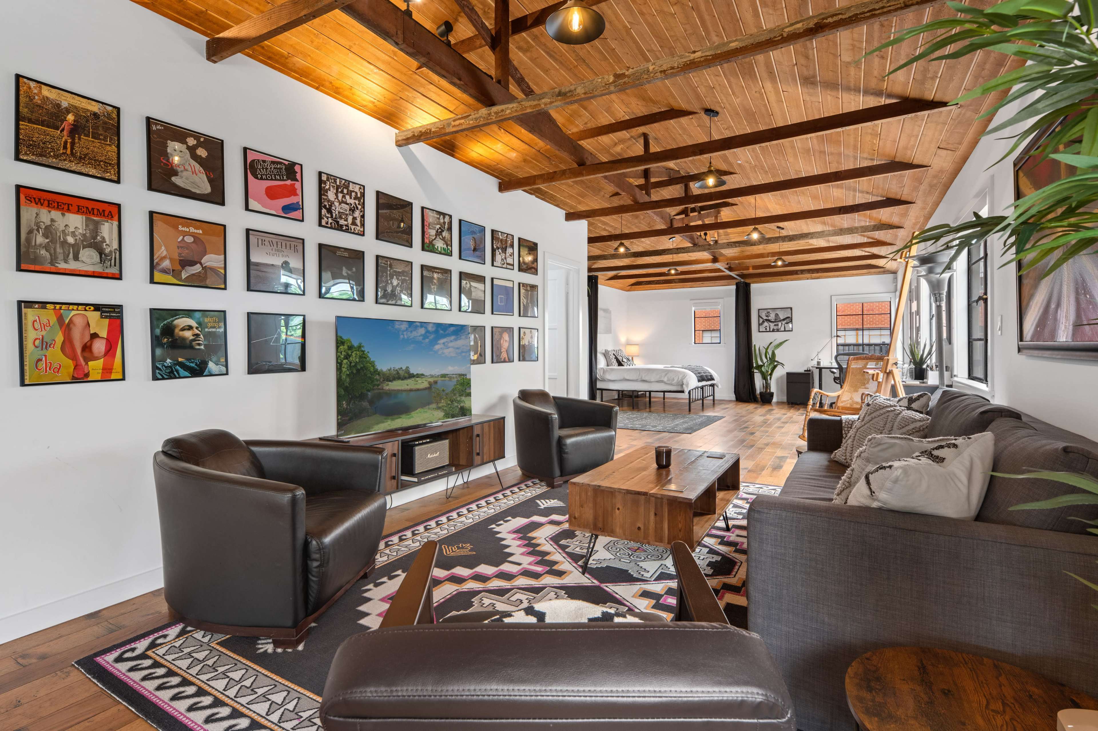 A stylish living space with wooden beams, a large area rug, comfortable seating, and an assortment of framed artwork on the walls.