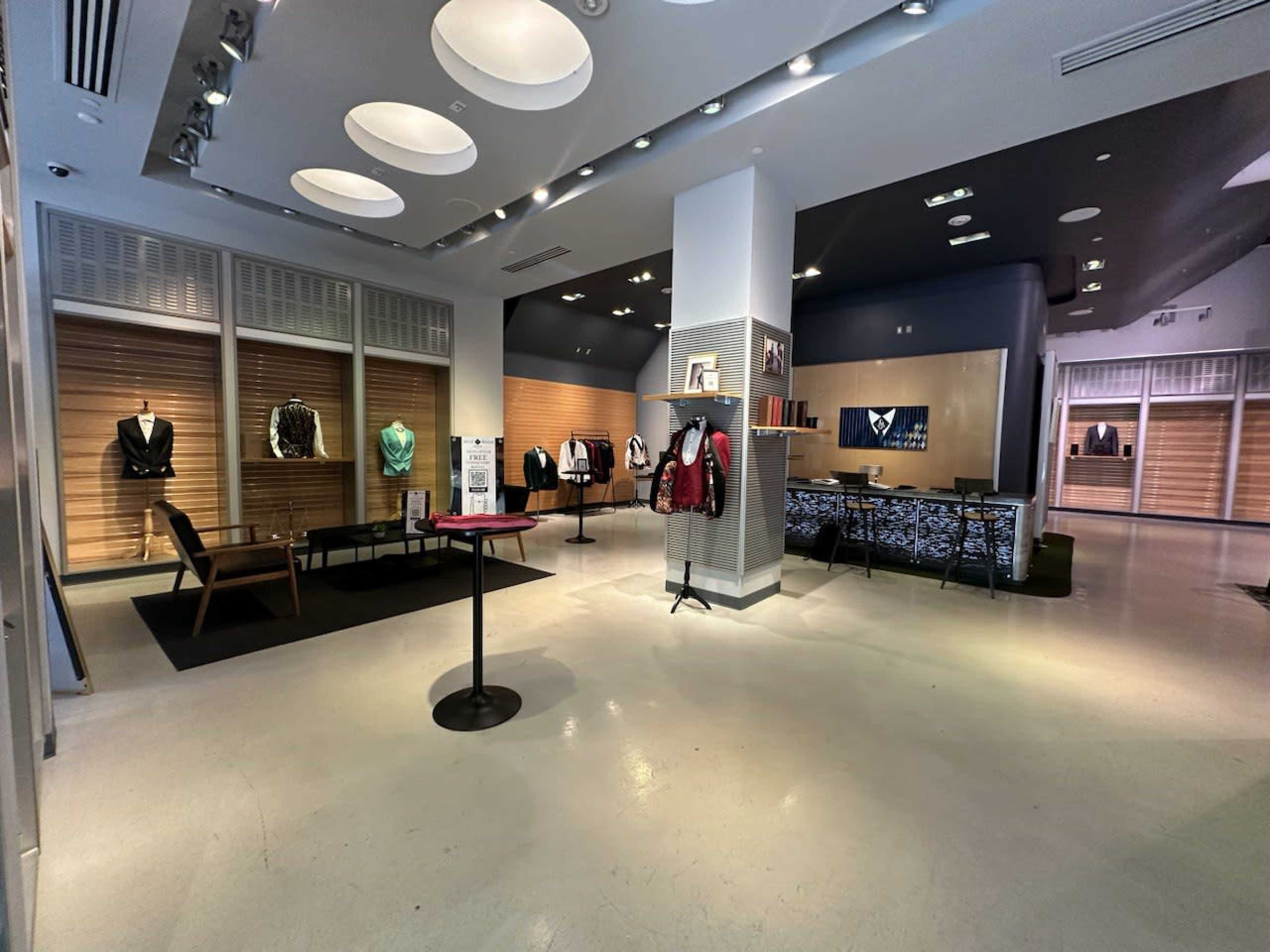 The image shows a modern retail store interior with displays of clothing on mannequins and racks, featuring a minimalist design and soft lighting.