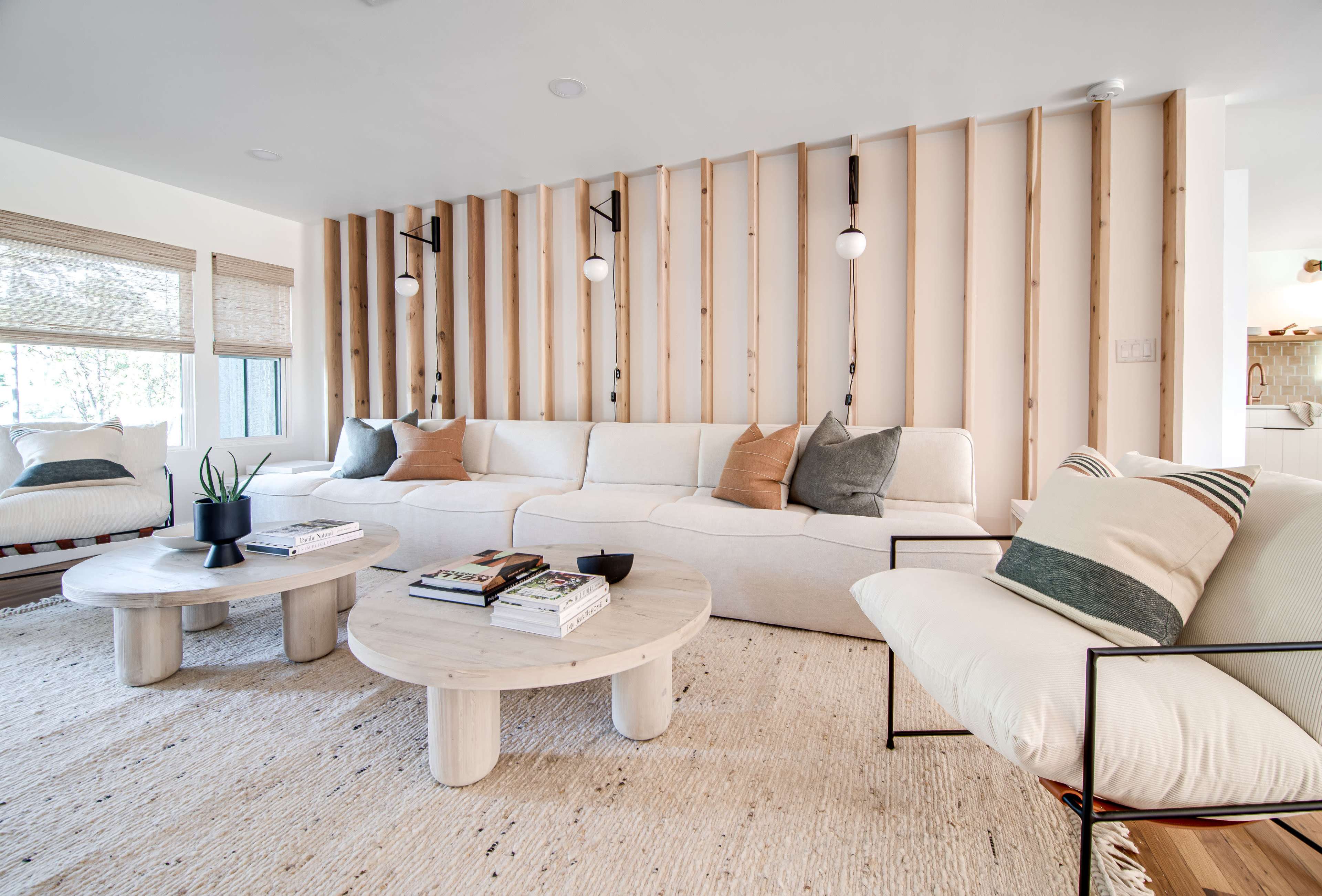 A modern living room with a sectional sofa, a round coffee table, and two accent chairs, all arranged around a textured rug against a backdrop of wooden wall slats.