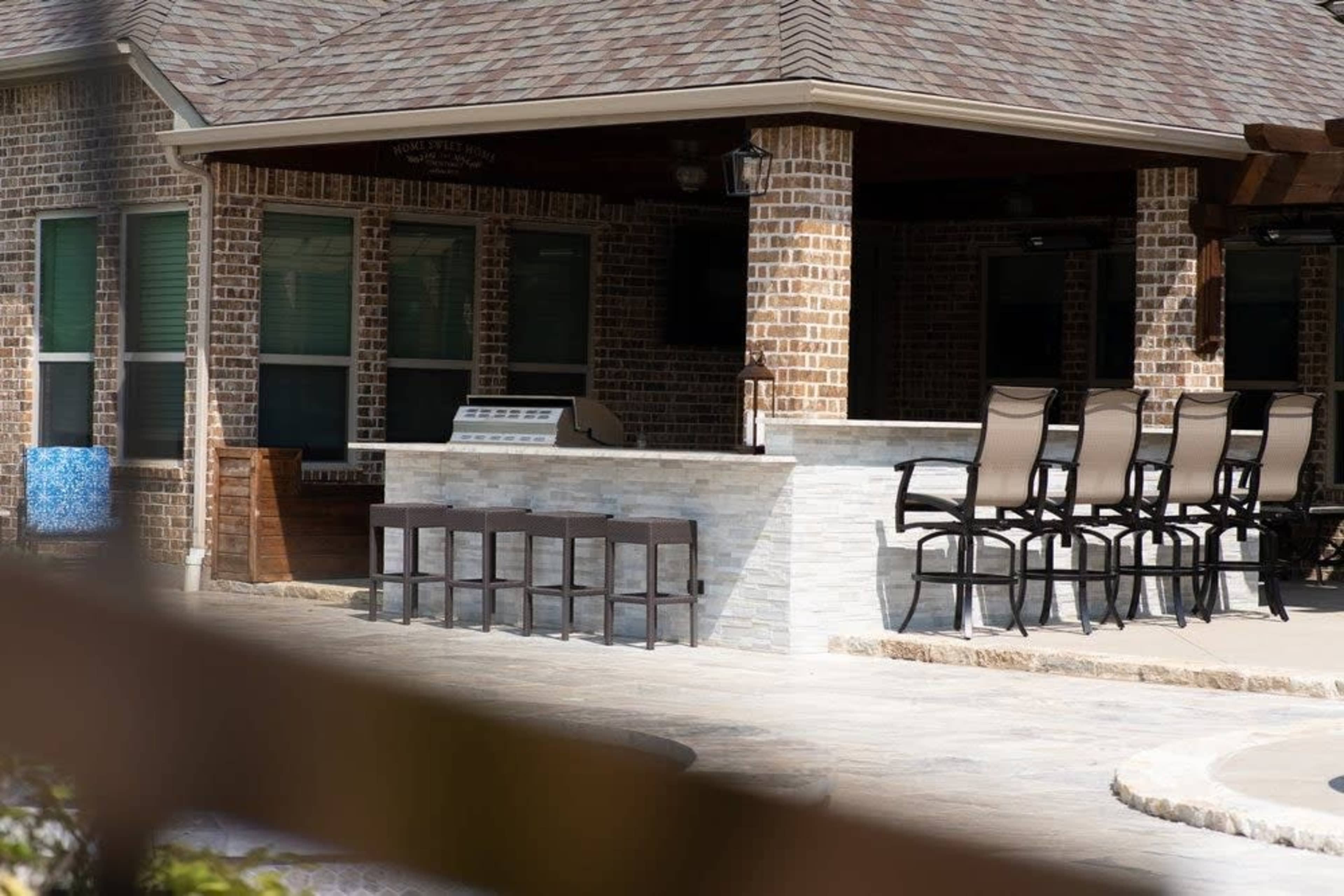 The image shows an outdoor bar area with high chairs arranged in front of a stone counter, set within a brick building.