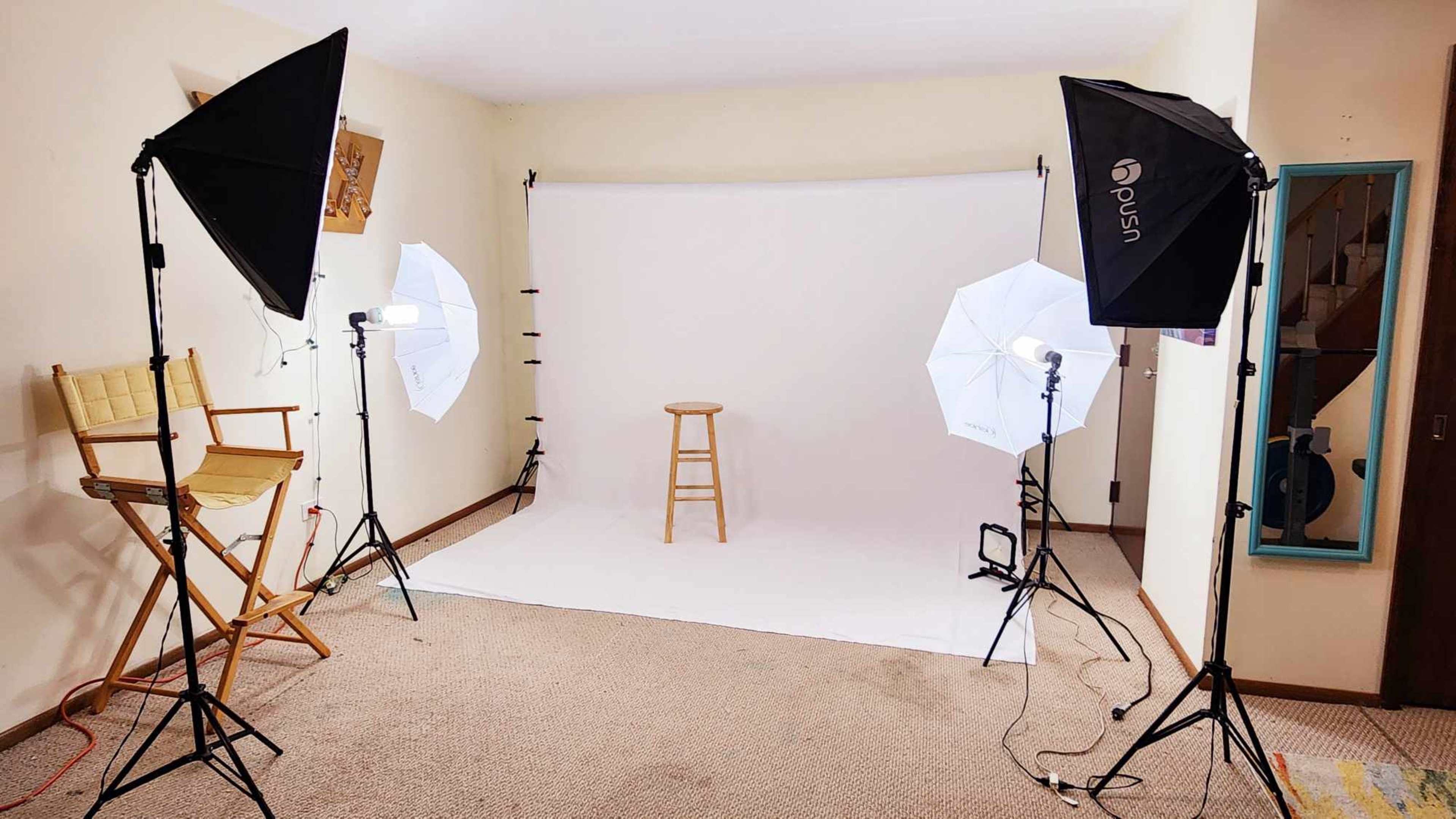 A photography setup with two softbox lights, a stool, and a backdrop in a room with beige walls and carpet.