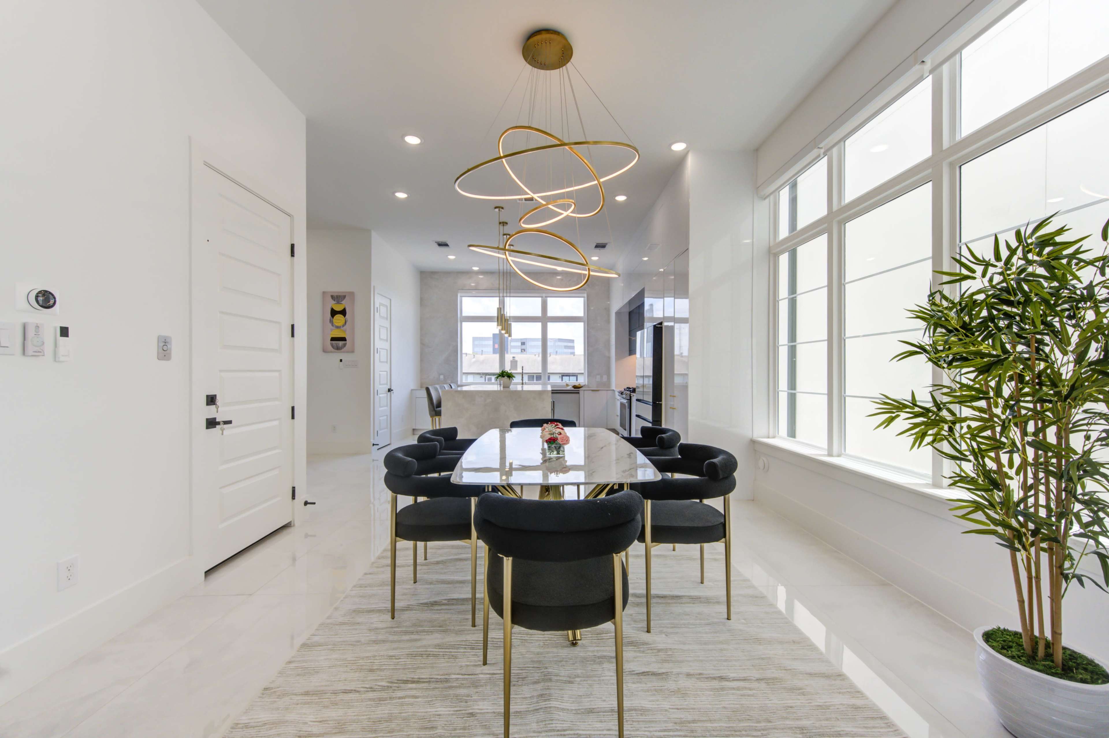 A modern dining area features a long table surrounded by black chairs, with a large window and a stylish light fixture overhead.