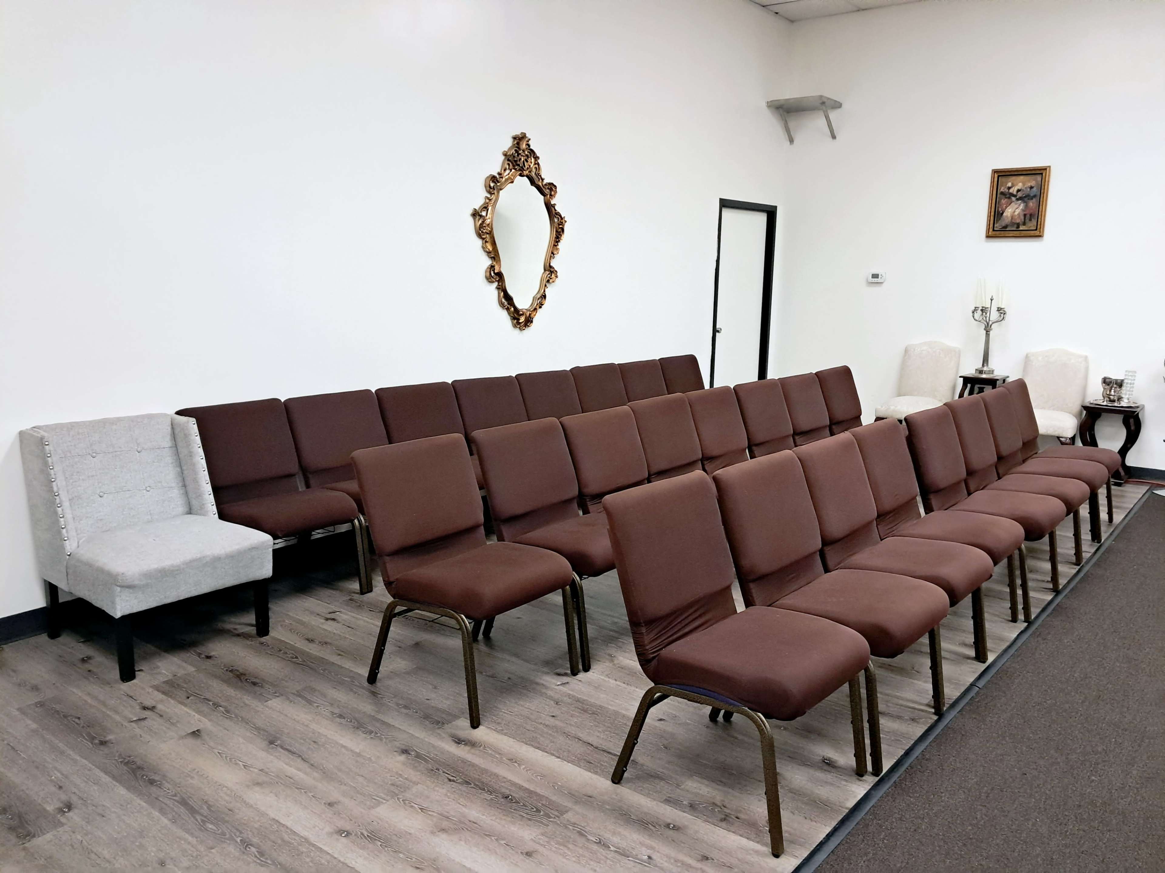 The image shows a neat row of brown chairs arranged in a waiting area, with a small gray chair and wall decor visible in the background.