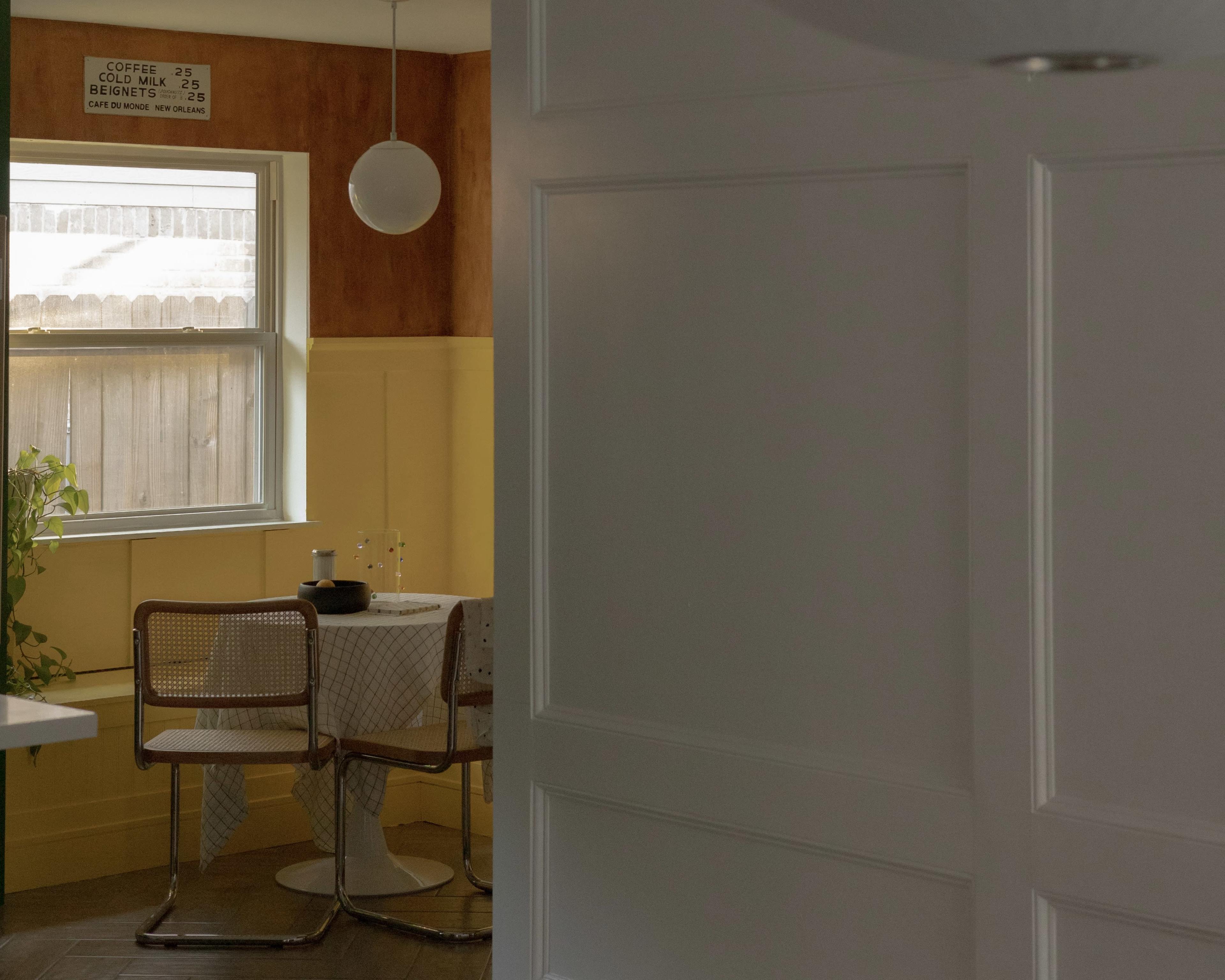 A small dining area features a table with a checkered tablecloth, two chairs, and a window letting in natural light.