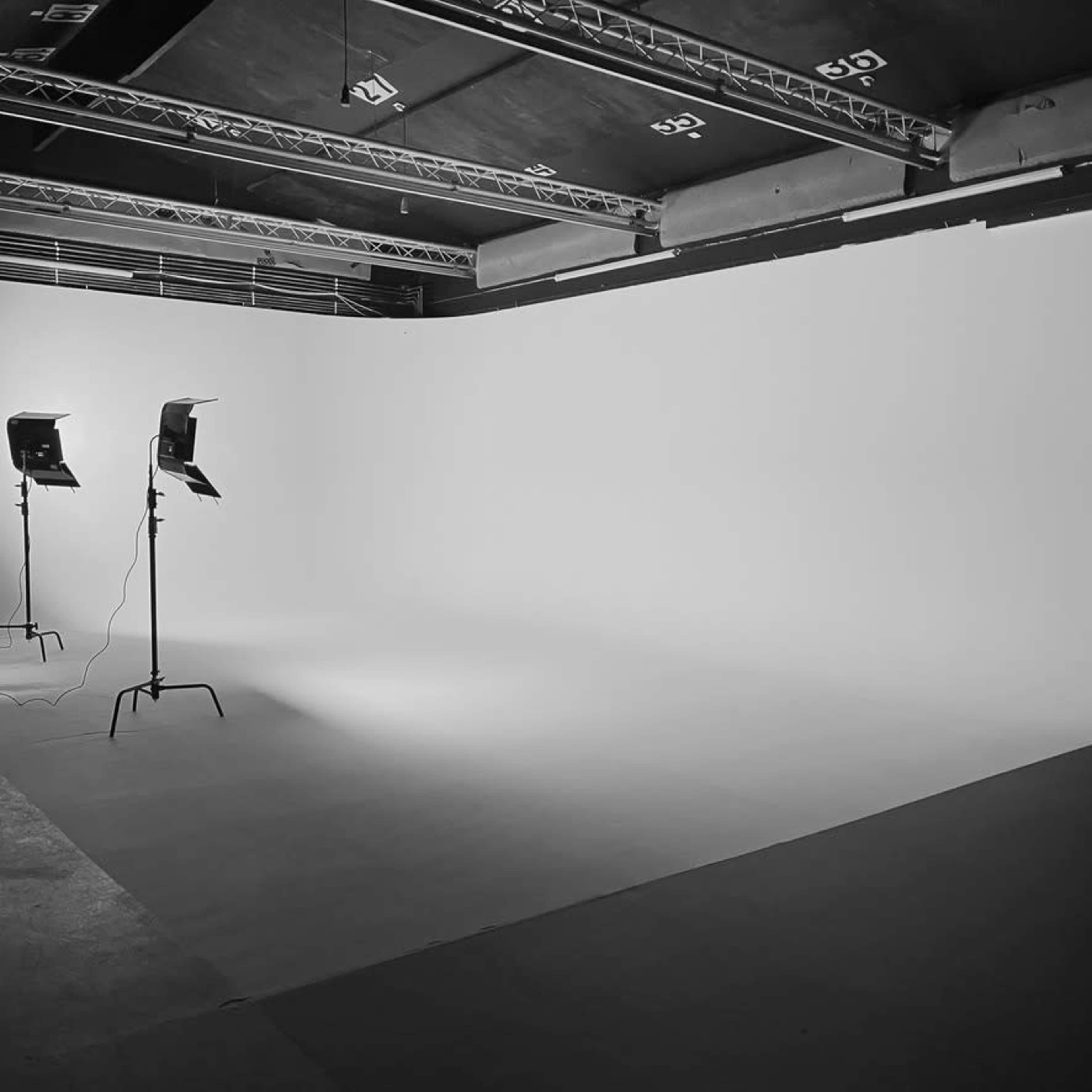A photography studio with two lighting stands and a large white backdrop.