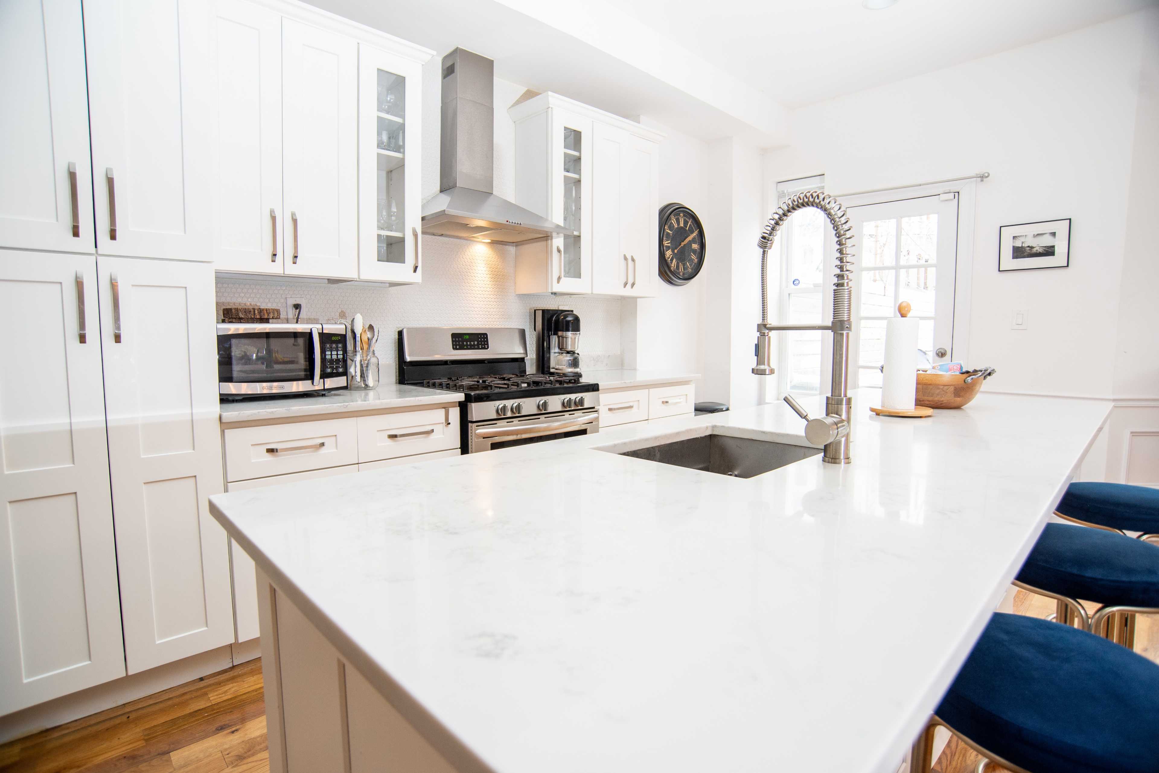 A modern kitchen features white cabinetry, a large island with a sink, stainless steel appliances, and bar stools.