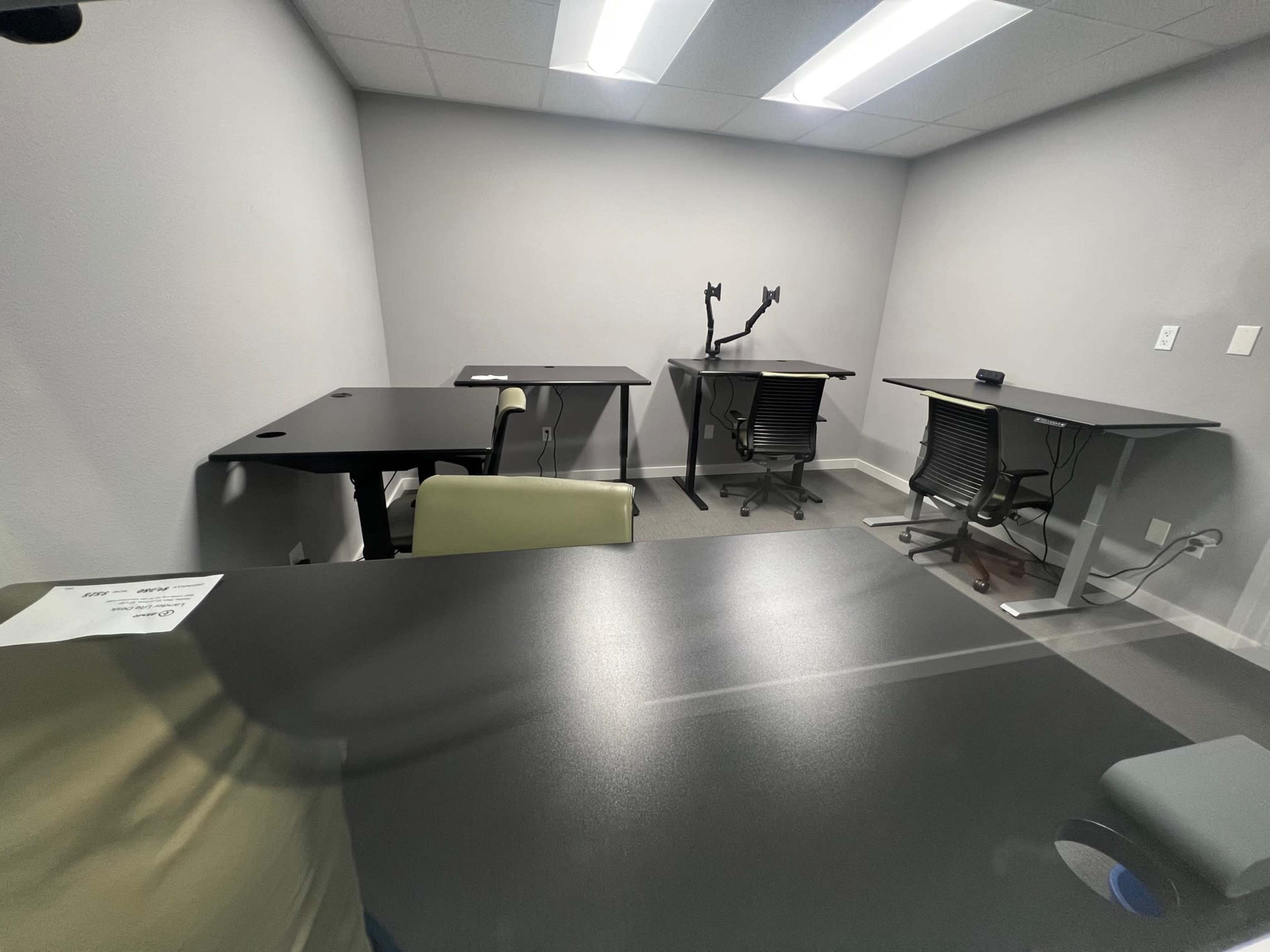 A small room with four desks and chairs arranged, two of which are standing desks.