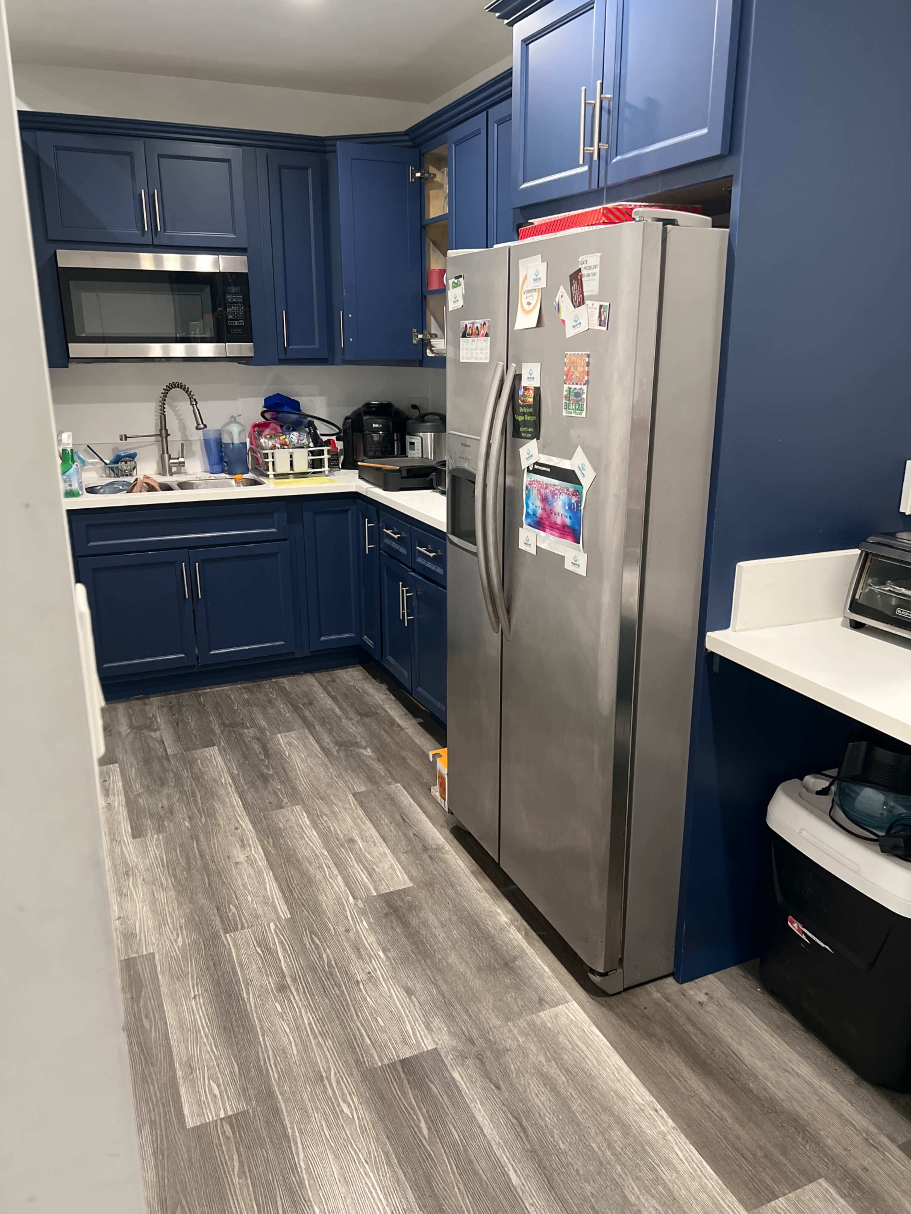 A modern kitchen with blue cabinets, stainless steel appliances, and a mix of countertop items and organizational containers.