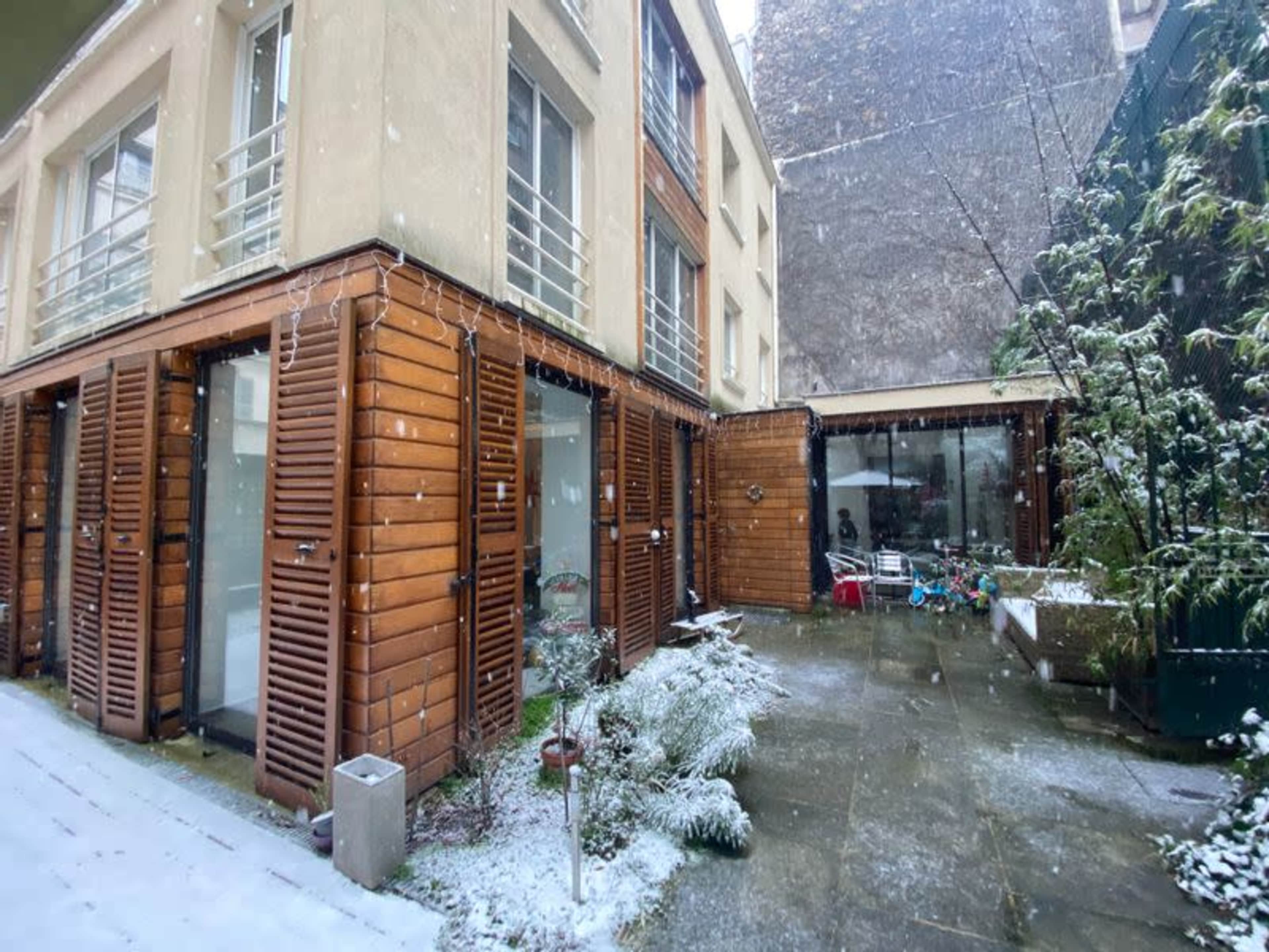 A snow-covered courtyard surrounded by buildings with wooden shutters and a glass-enclosed area.