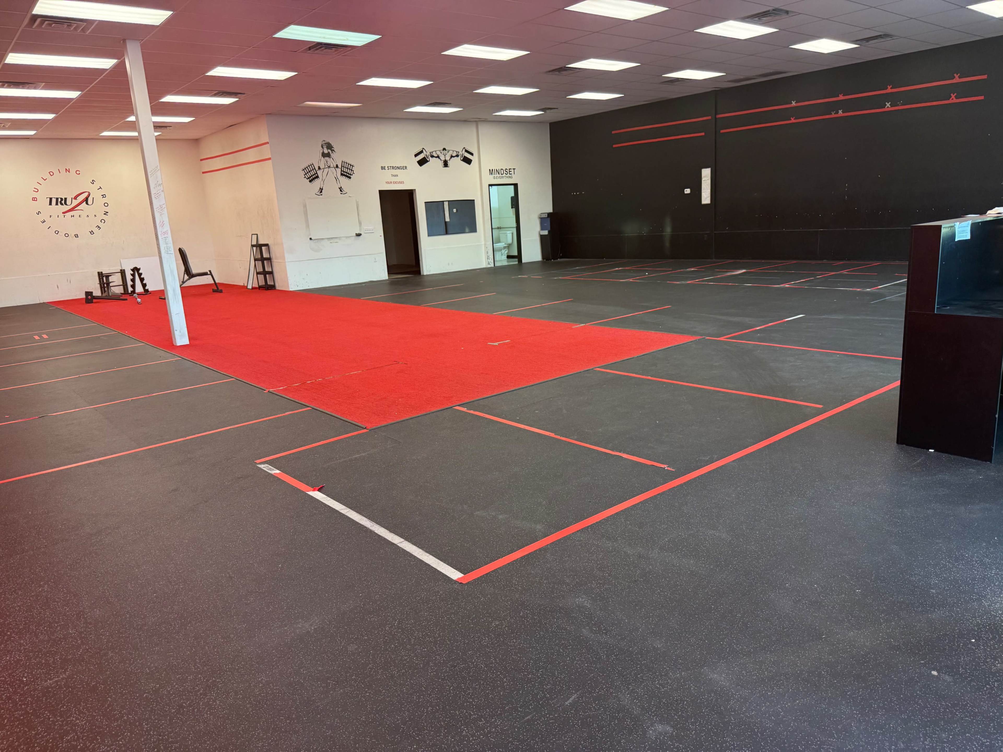 The image shows a spacious gym area with red and black flooring, marked out with red lines indicating workout stations and equipment placement.