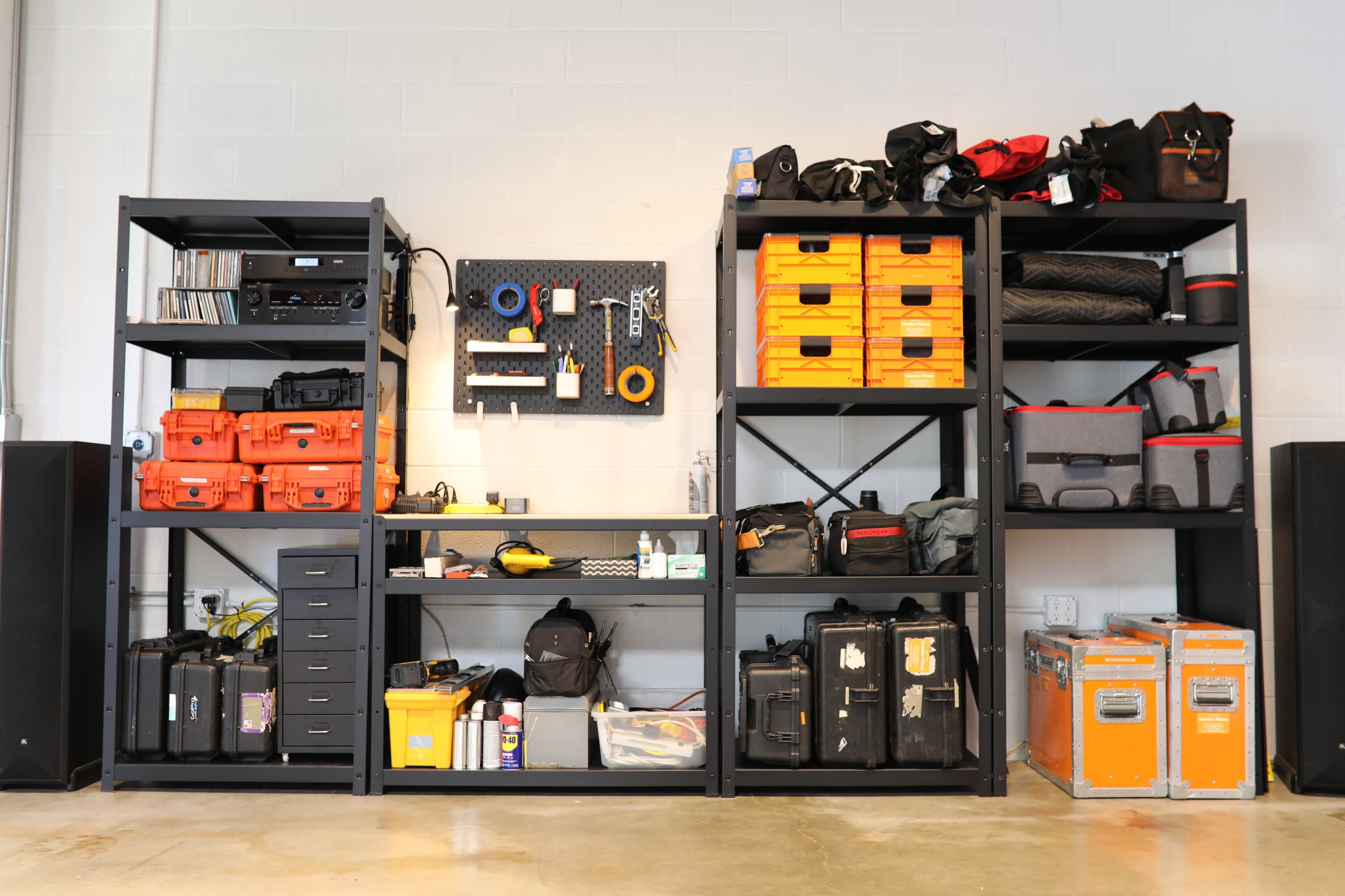 A well-organized workshop area with black shelving units filled with various toolboxes, storage containers, and equipment.