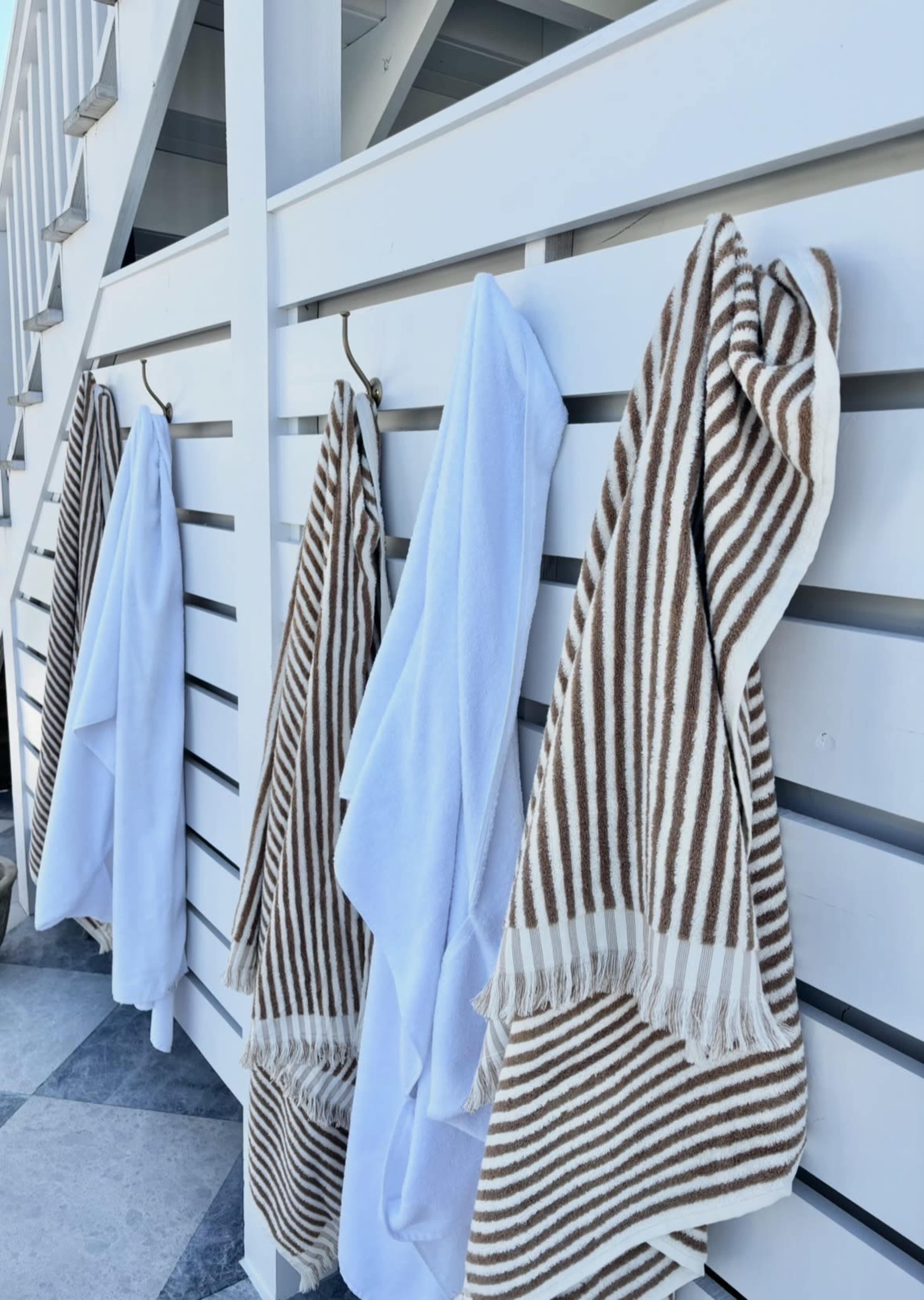 A set of striped and solid towels hangs neatly on hooks against a white wooden fence.