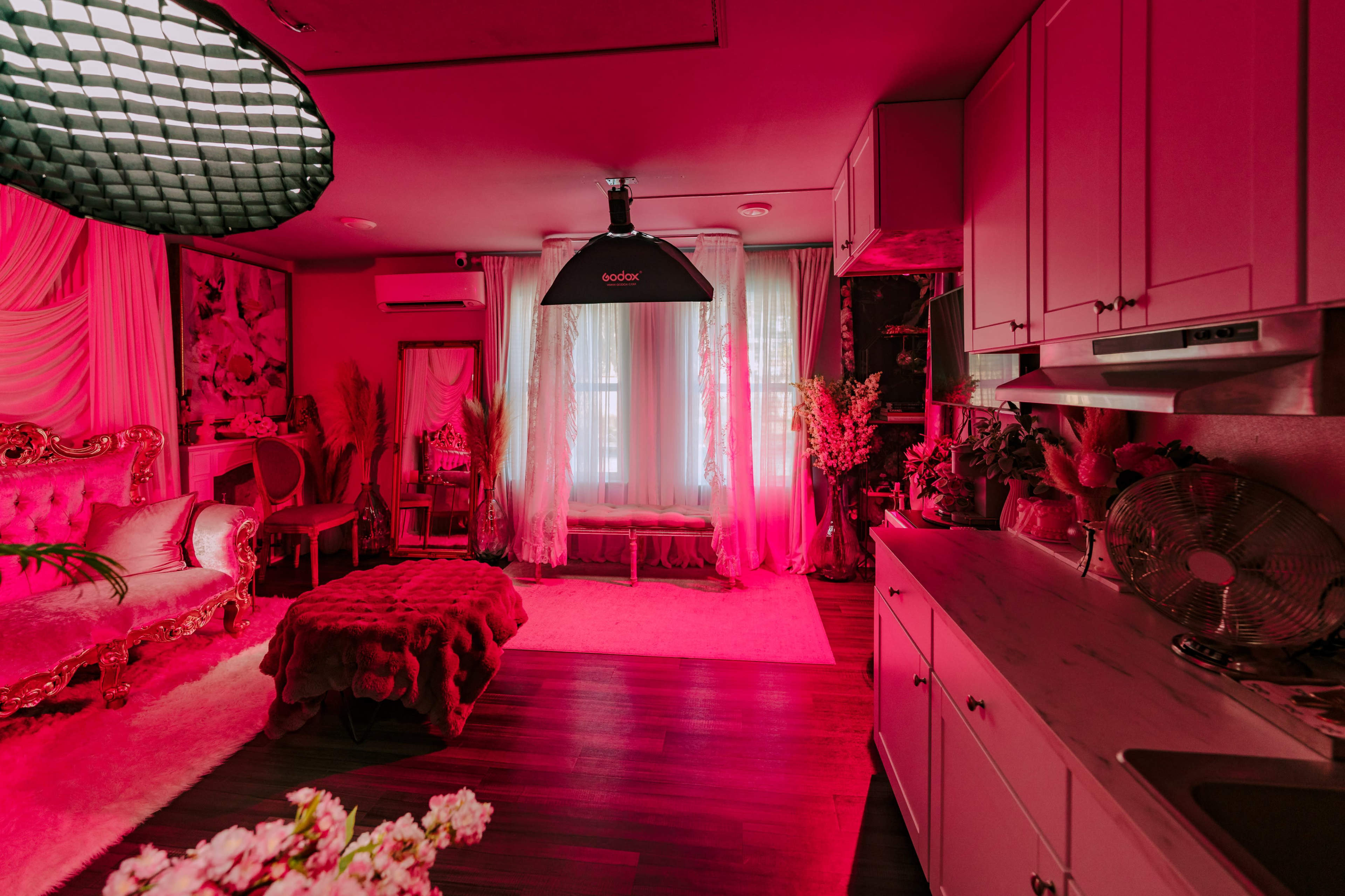 The room features pink lighting, a plush sofa, and decorative plants, creating a vibrant atmosphere.