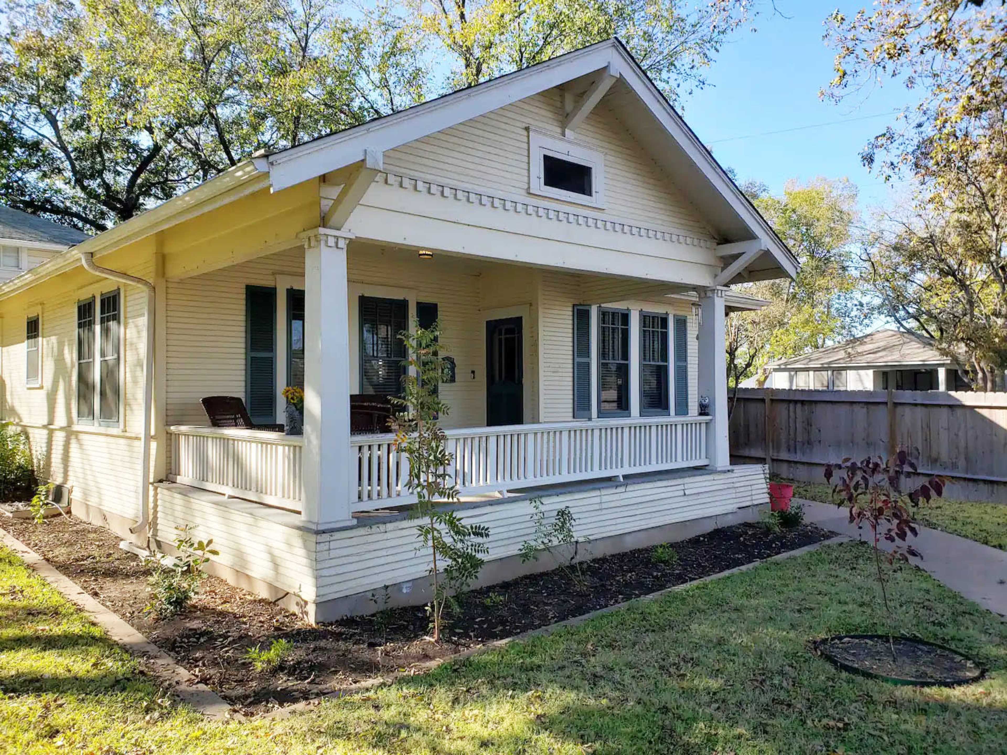 A single-story house with a covered porch, green shutters, and a well-maintained yard.