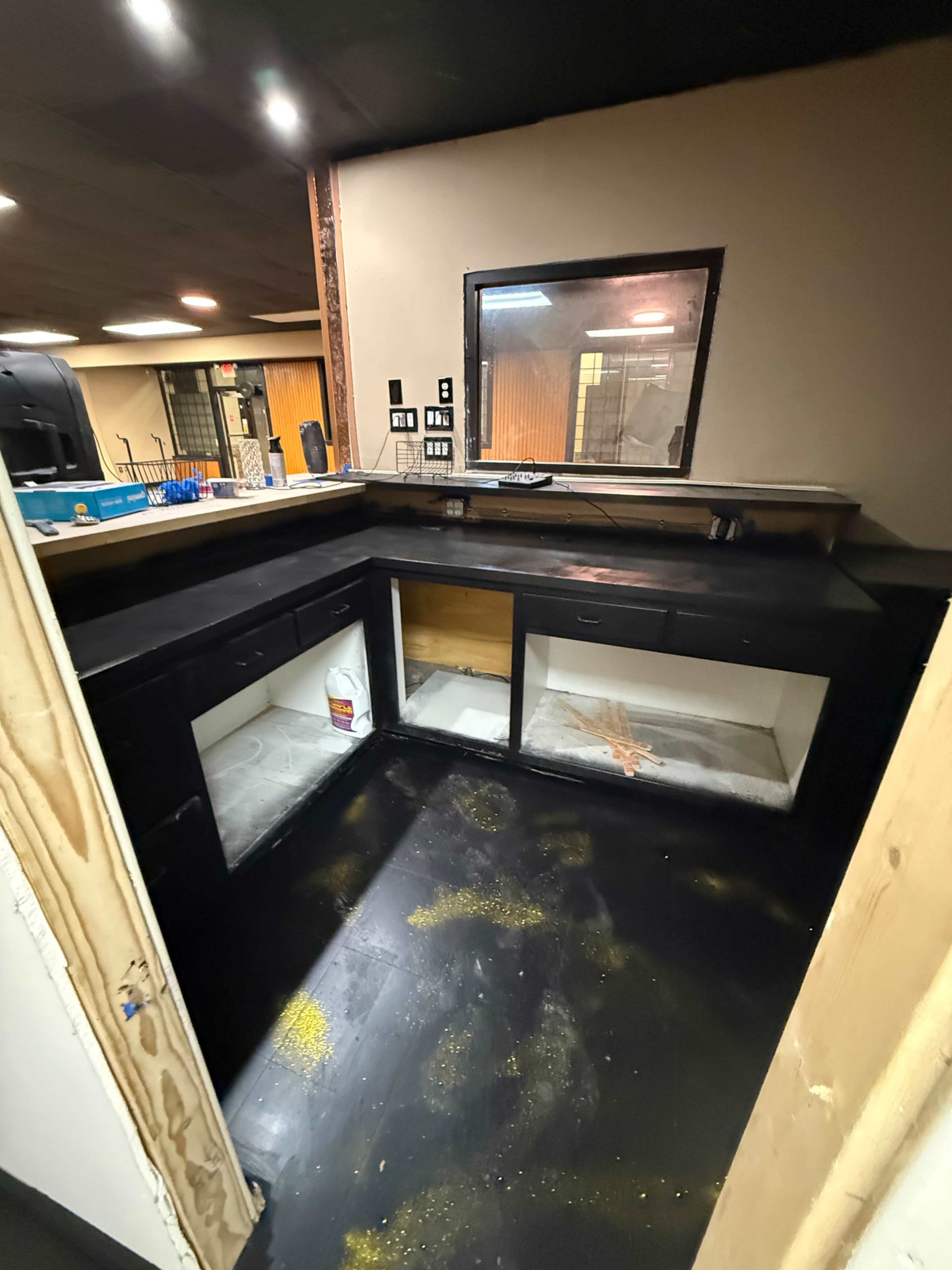 The image shows an unfinished area of a kitchen or bar with black cabinets and surfaces, featuring a partially installed countertop and scattered materials on the floor.